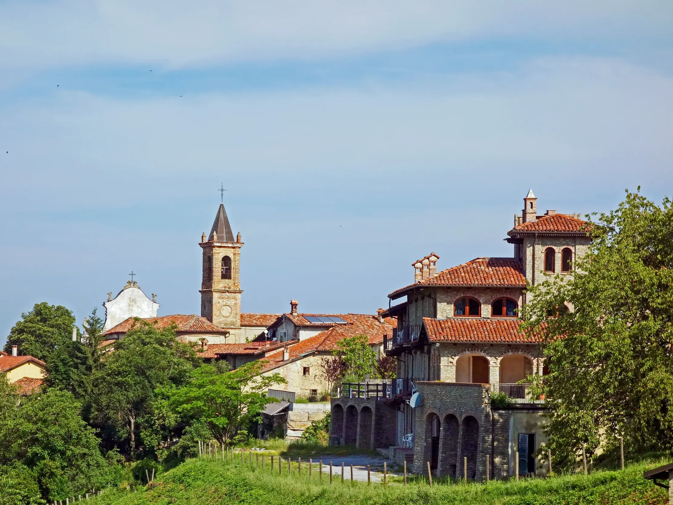 Malerisches Hügeldorf Monforte d'Alba mit Steinhäusern und Kirche, umgeben von grünen Hügeln der Langhe im Piemont.