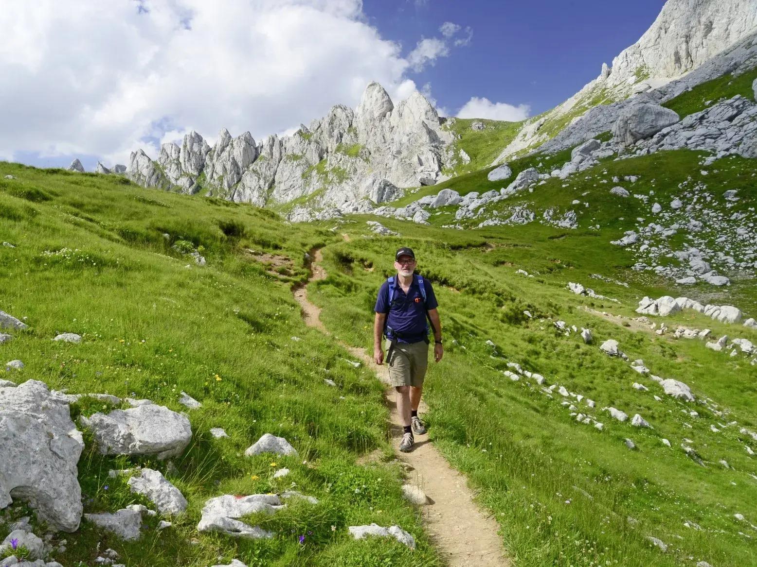Wanderer mit Rucksack auf einem schmalen Pfad im Durmitor Nationalpark vor der schroffen Gipfelkette Crvena Greda.