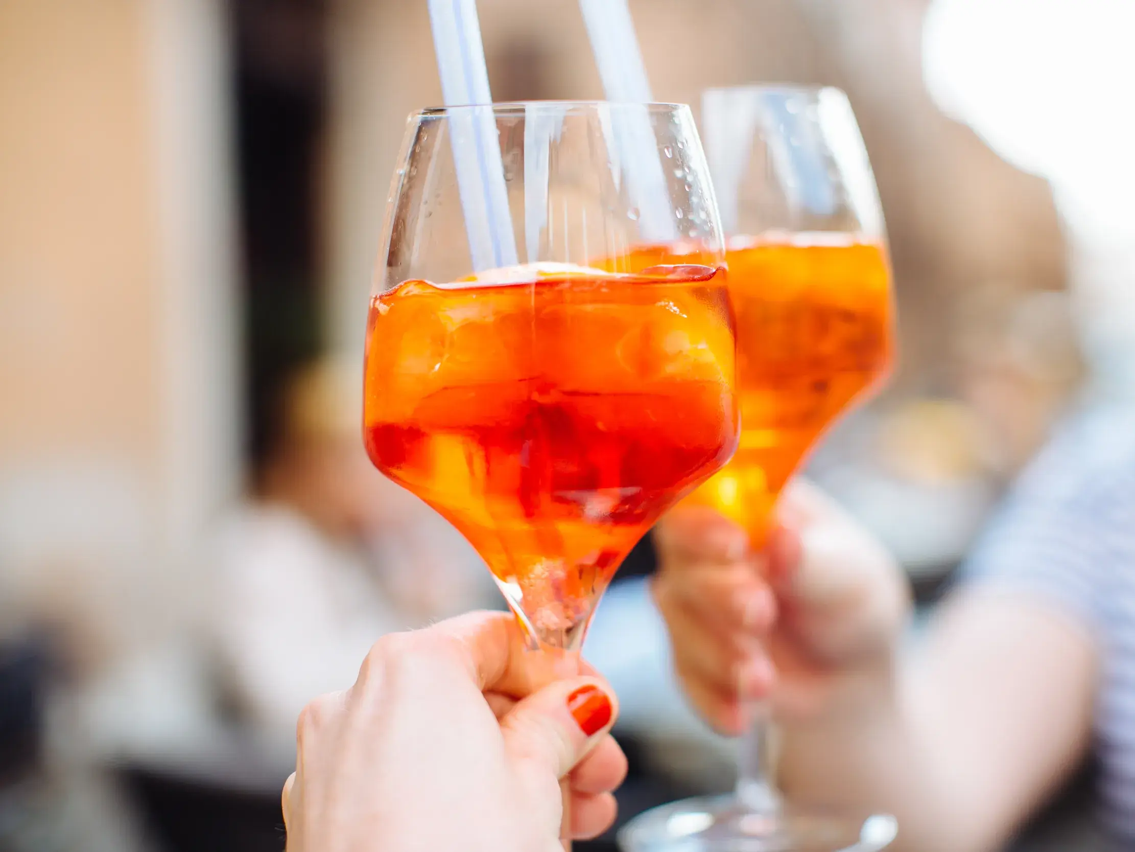 Nahaufnahme von zwei Personen, die in einem Café in Venetien mit Gläsern voll orangem Sprizz und Eiswürfeln anstoßen.