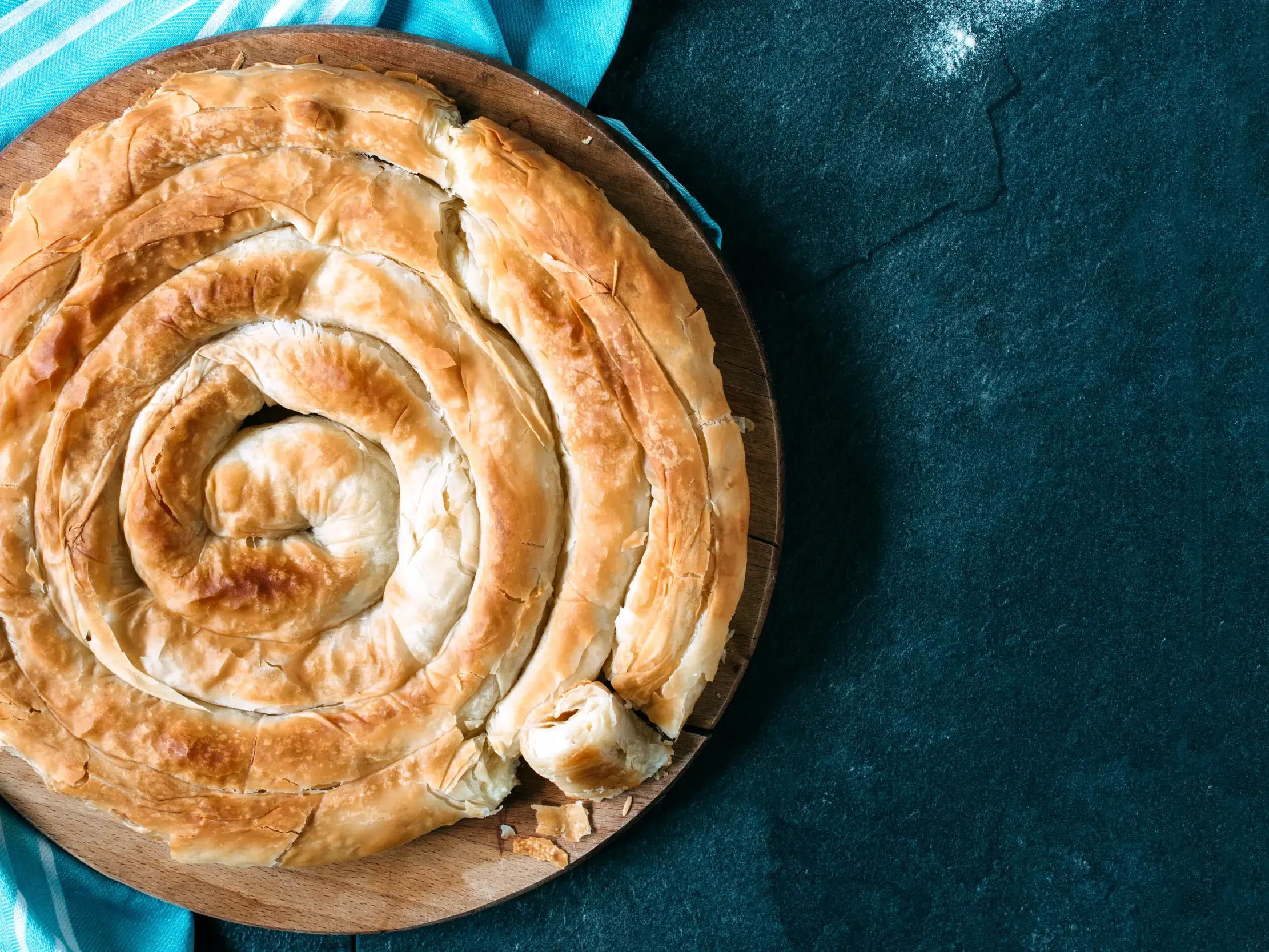 Eine traditionelle, spiralförmig gedrehte griechische Pita, frisch aus dem Ofen auf einem rustikalen Holzbrett angerichtet.