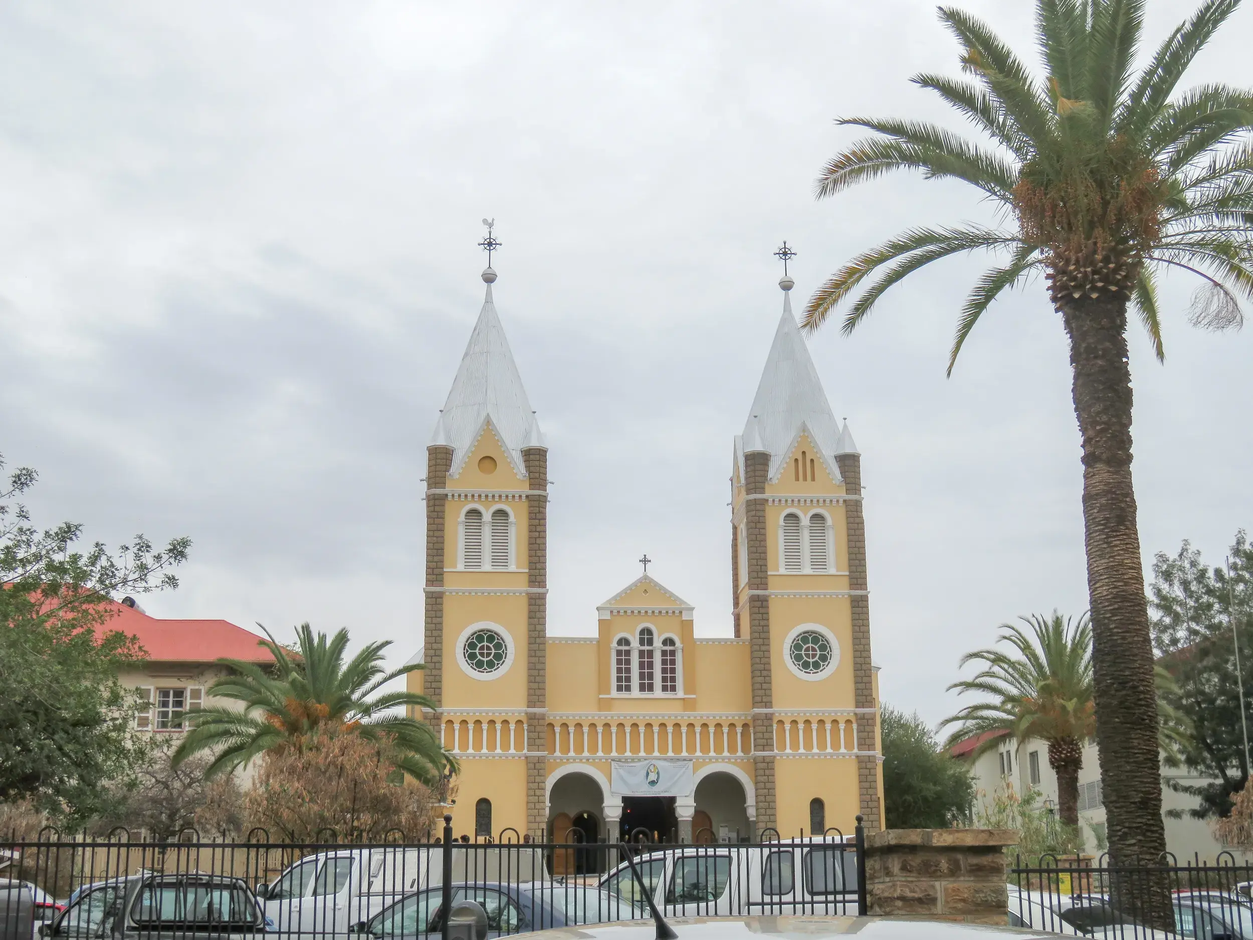 Die Christuskirche in Windhoek, ein Wahrzeichen Namibias, mit gelber Fassade und weißen Turmspitzen neben einer Palme.