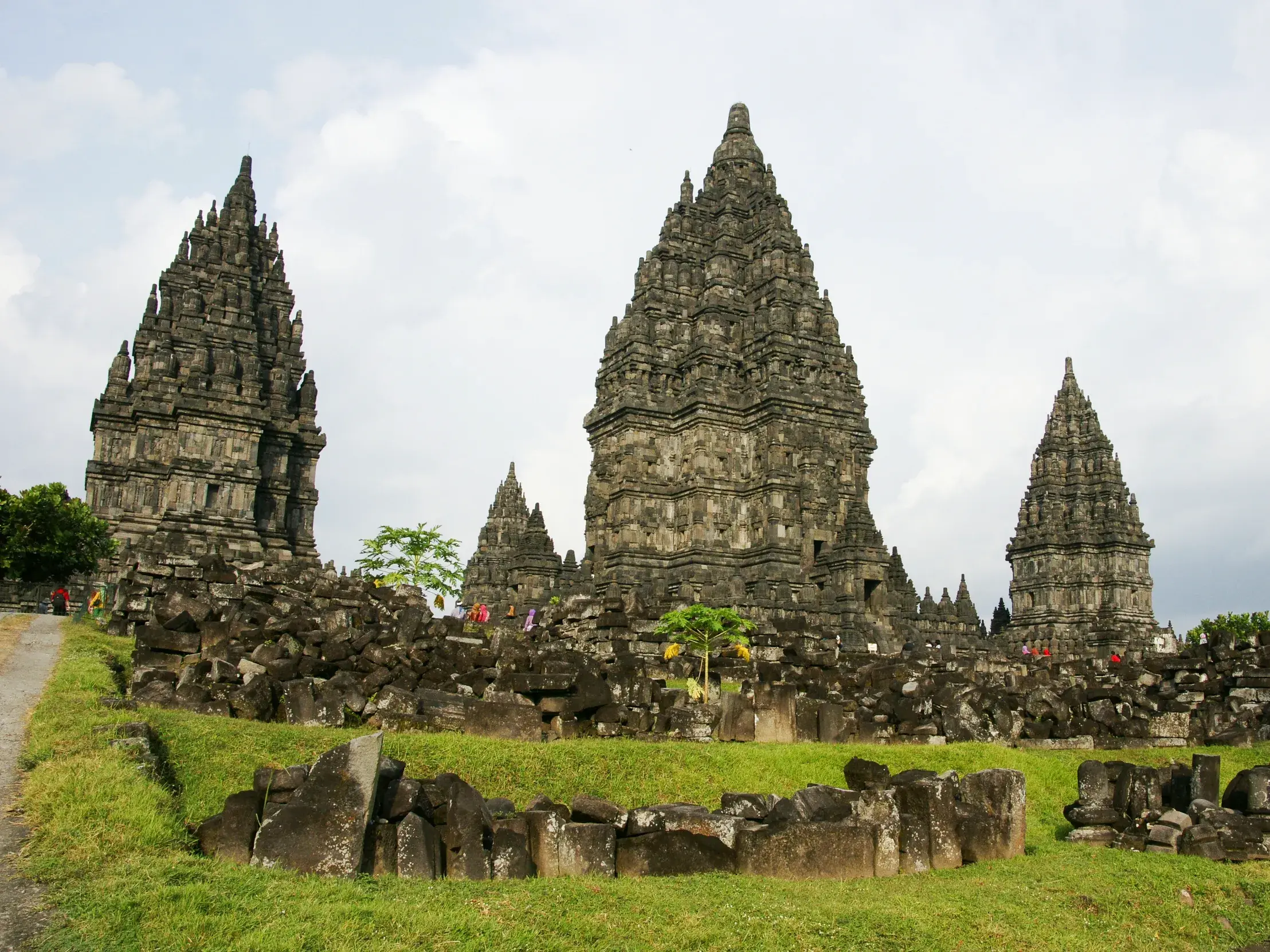 Die spitzen Türme des UNESCO-Weltkulturerbes Prambanan auf Java, umgeben von grünen Wiesen und steinernen Ruinen.
