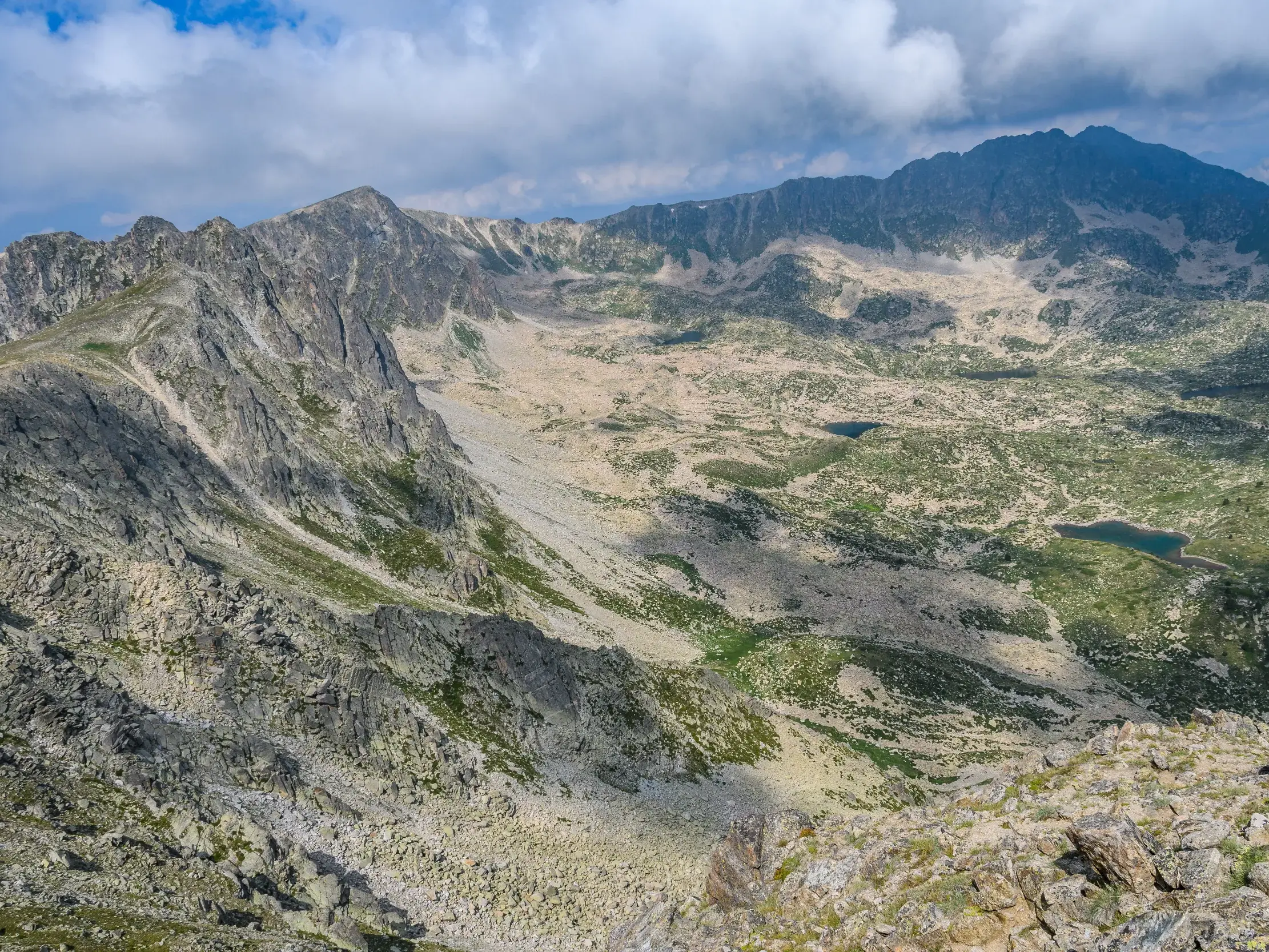 Panoramablick vom Gipfel des Pic de Montmalús auf die karge Hochgebirgslandschaft mit kleinen Karseen in Andorra.