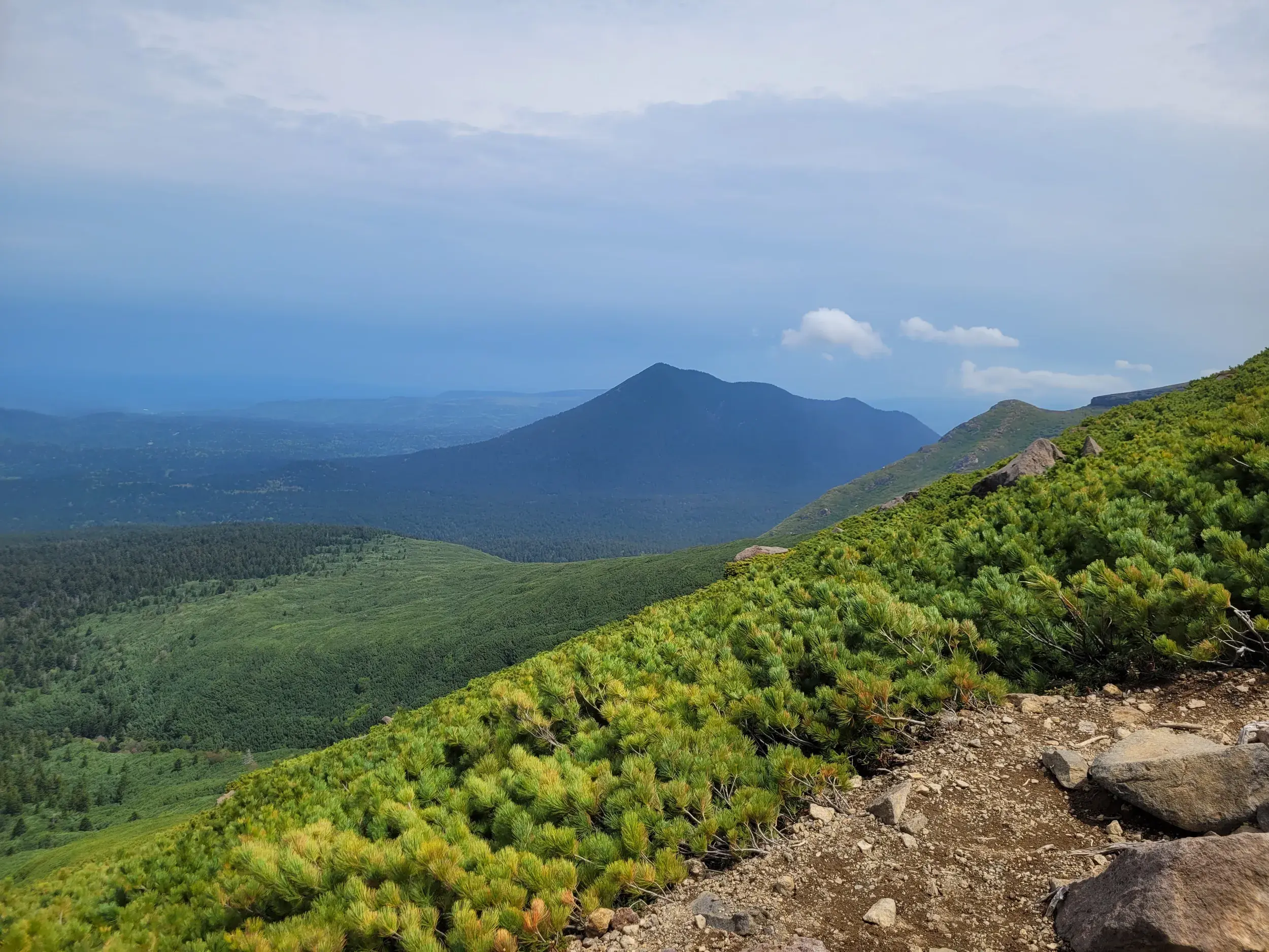 Steiniger Wanderpfad am Vulkan Meakan-dake mit Panoramablick über die grüne Berglandschaft des Akan Nationalparks.