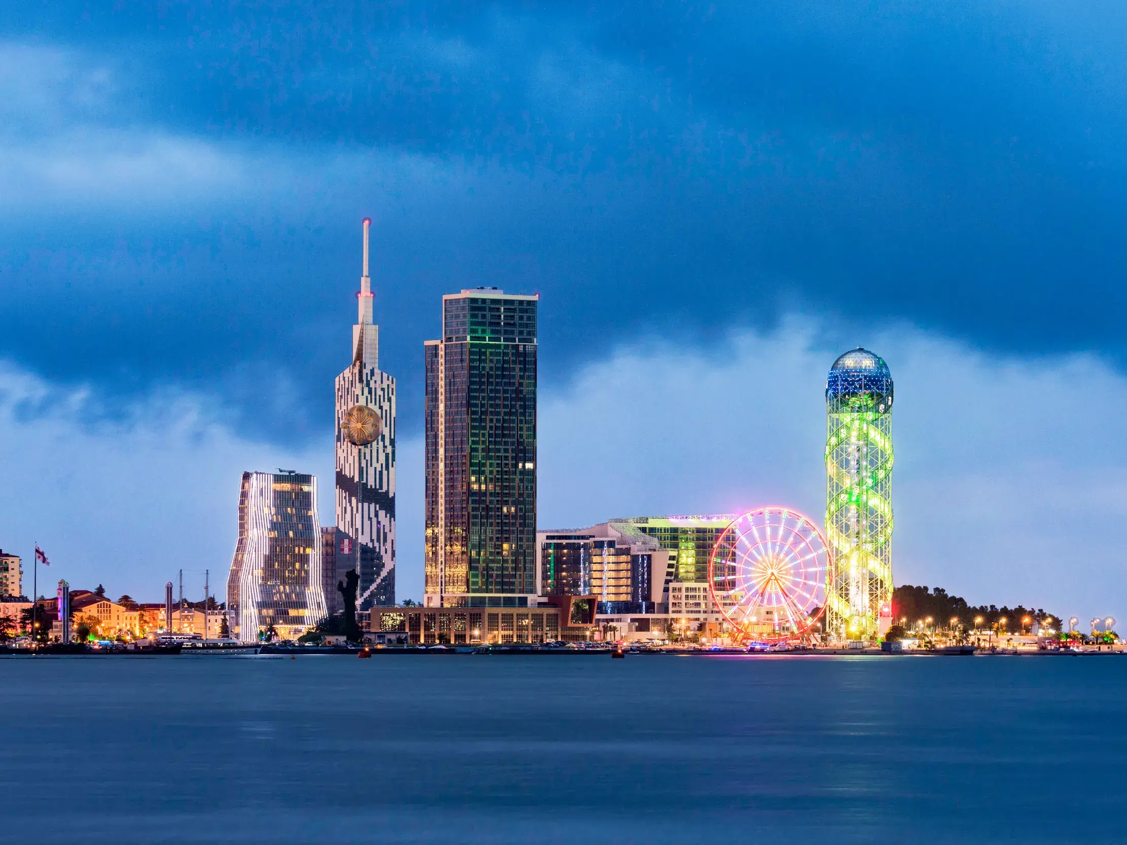 Die beleuchtete Skyline von Batumi mit dem Alphabetic Tower und Riesenrad am Schwarzen Meer während der blauen Stunde.