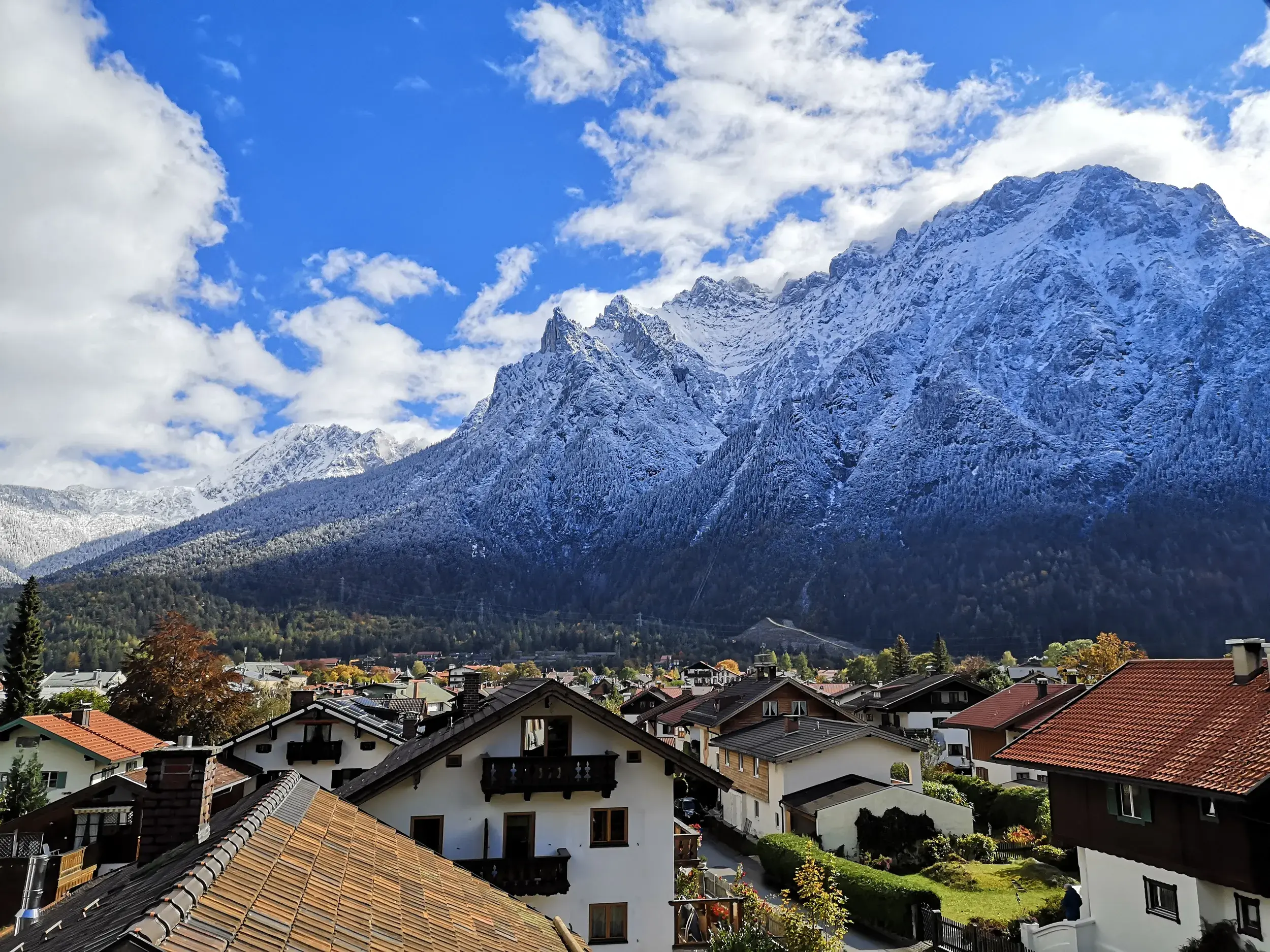 Blick über die Dächer von Mittenwald auf die schneebedeckten Gipfel des Karwendelgebirges unter blauem Himmel.