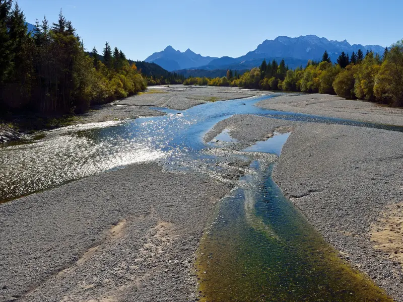 Weite Wildflusslandschaft der Isar bei Wallgau mit sonnen-glitzerndem Wasser und Blick auf das Karwendelgebirge.
