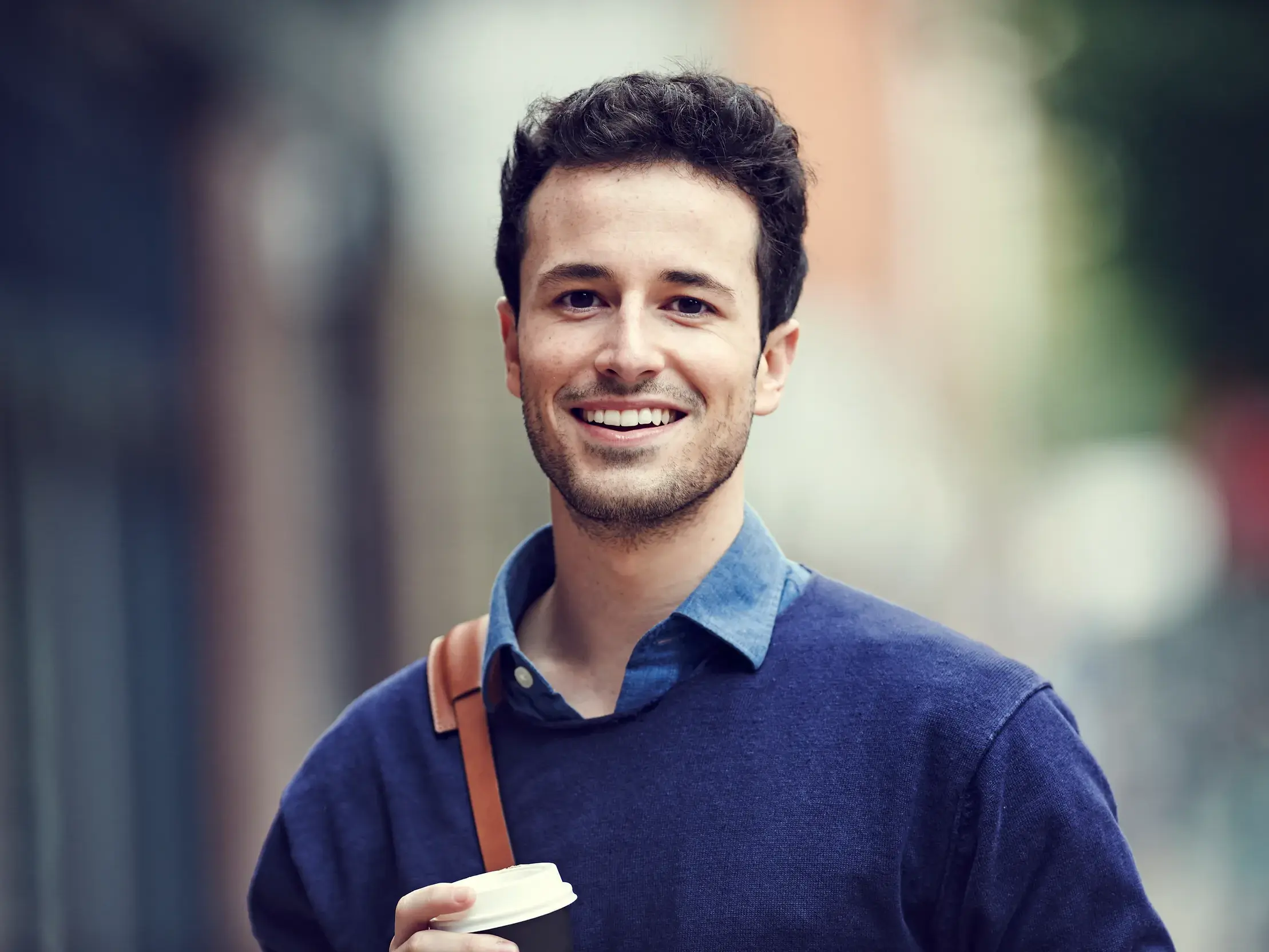Ein junger Student lächelt in die Kamera, während er mit einem Kaffee durch die Straßen von Tirana in Albanien geht.