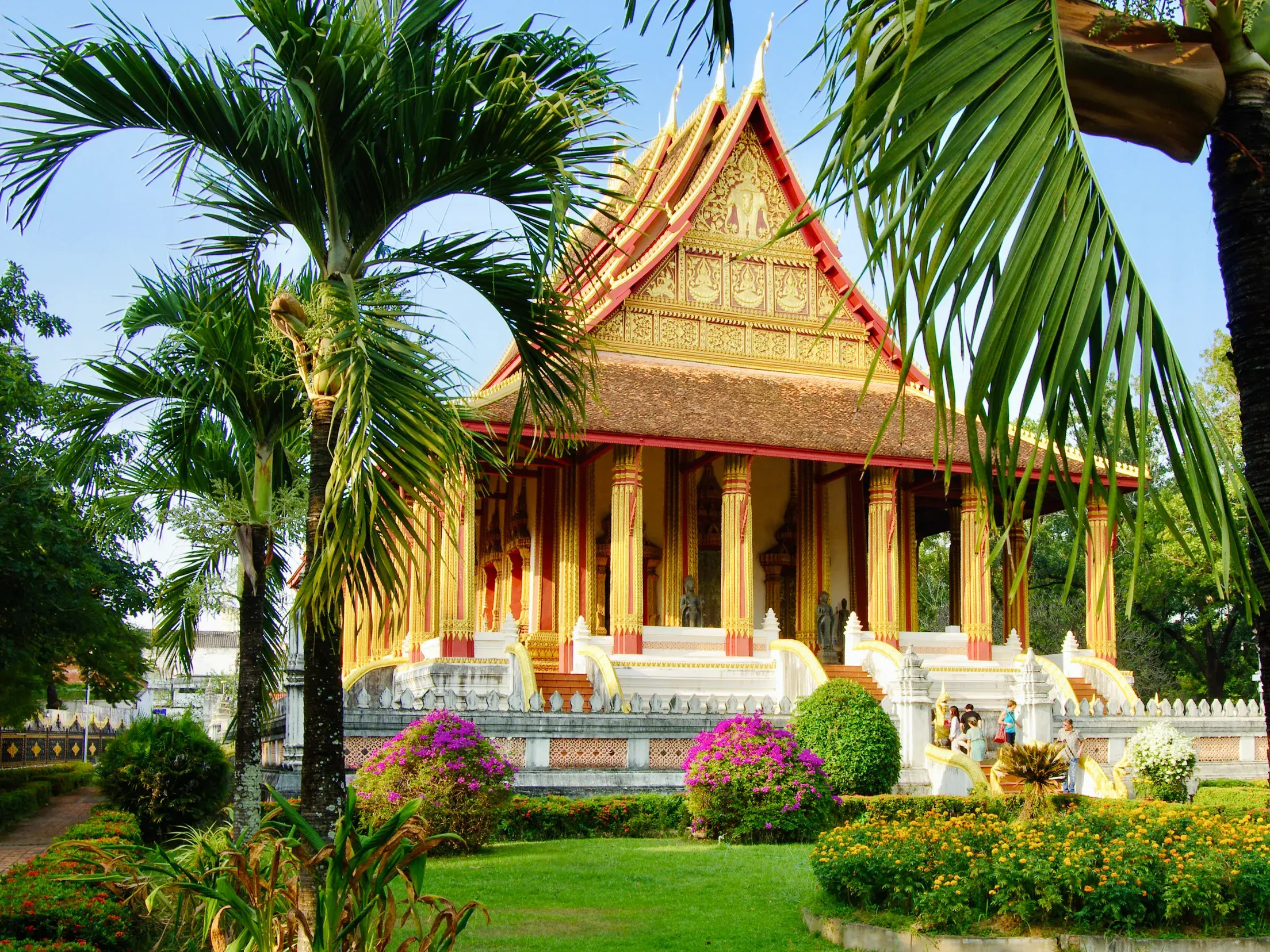 Der prachtvolle Ho Phra Kaeo Tempel in Vientiane, Laos, umgeben von einem tropischen Garten mit Palmen und blühenden Büschen.