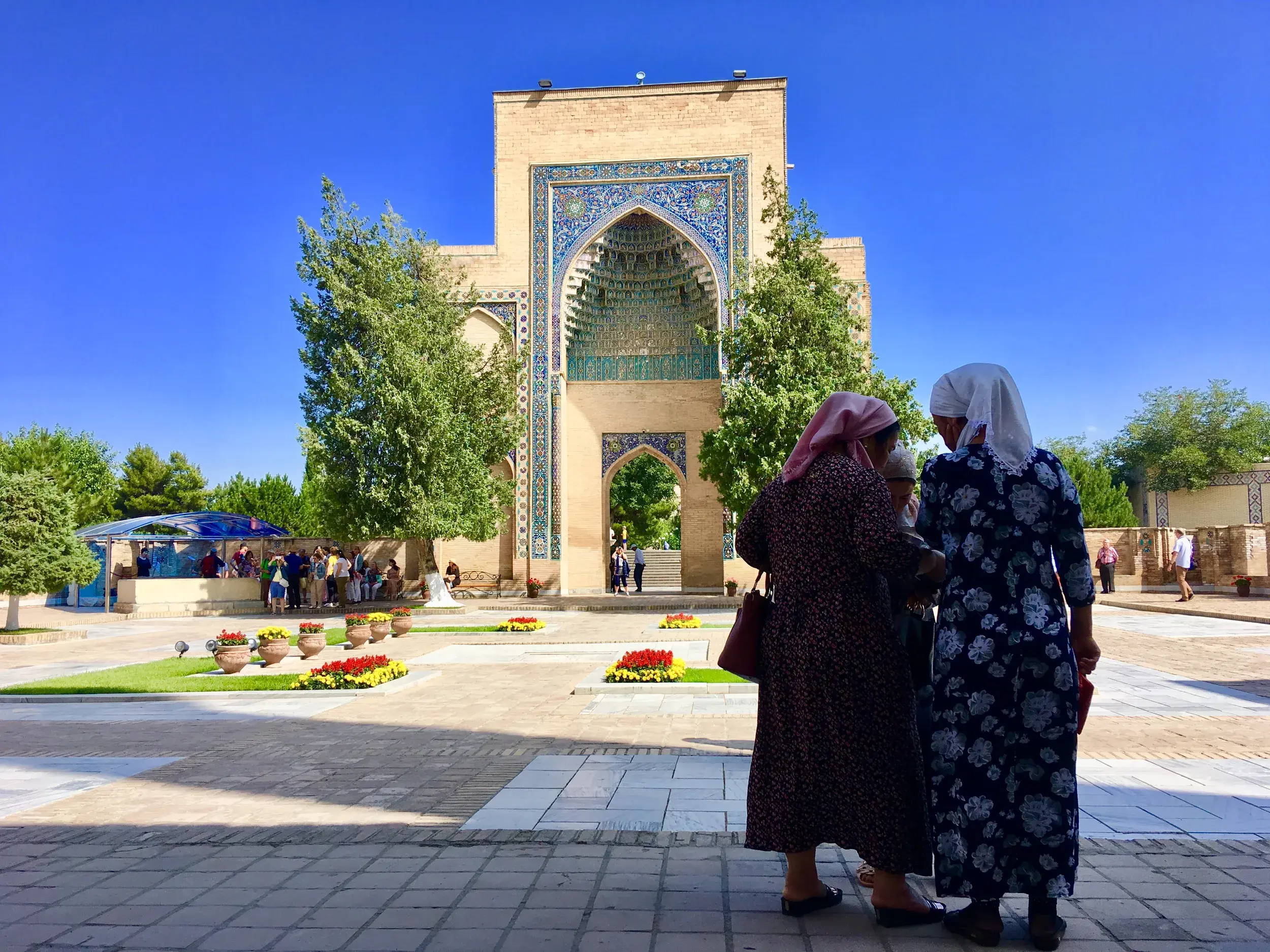 Einheimische Frauen in traditioneller Kleidung vor dem mit blauen Mosaiken verzierten Bakhautdin-Naqshband-Komplex bei Buchara.