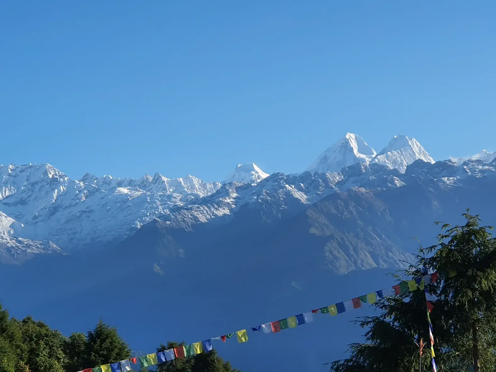 Bunte Gebetsfahnen flattern vor der majestätischen, schneebedeckten Bergkette des Jugal Himal bei einer Trekkingreise in Nepal.