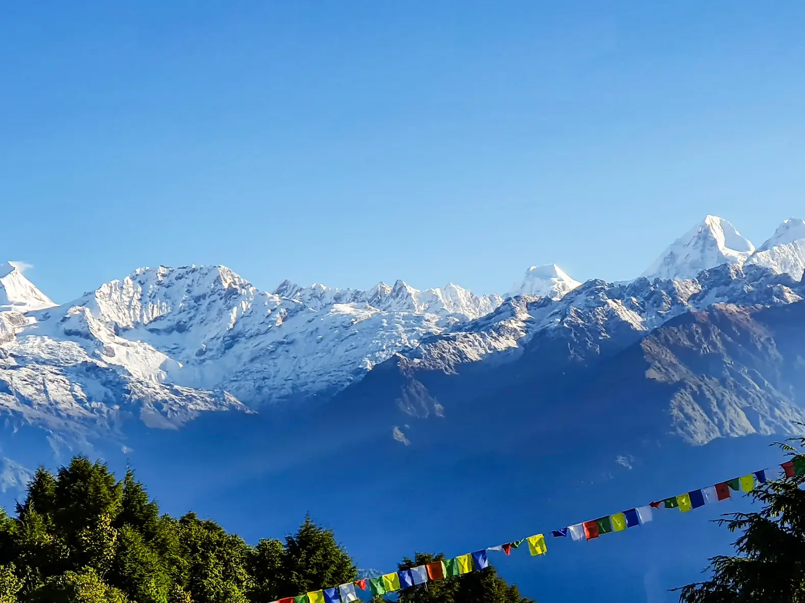 Bunte Gebetsfahnen im Vordergrund einer weiten, schneebedeckten Bergkette des Jugal Himal in Nepal unter klarem Himmel.
