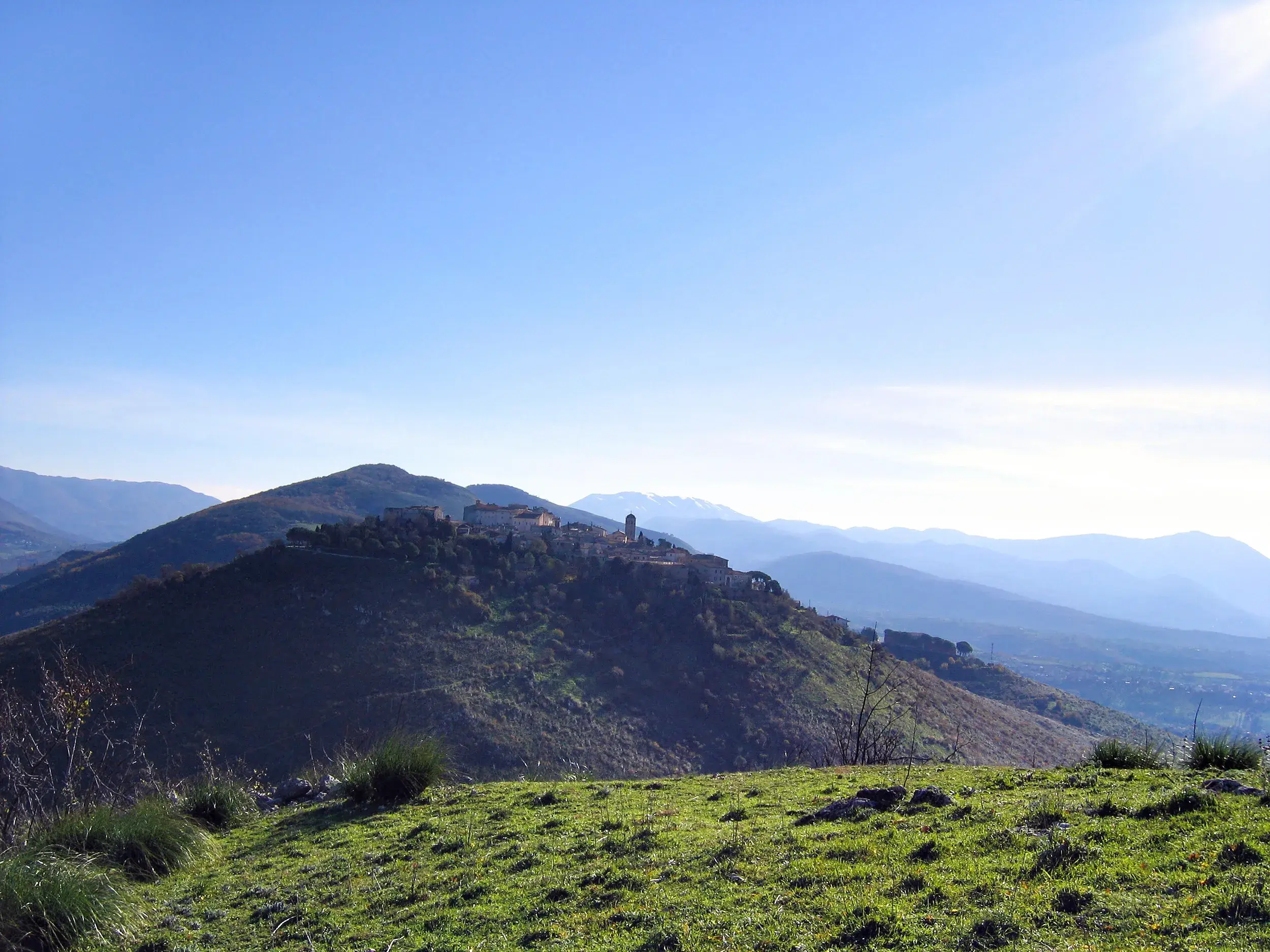 Blick von einer Wanderung auf das Bergdorf Montemonaco, das auf einem grünen Hügel im Nationalpark Monti Sibillini liegt.