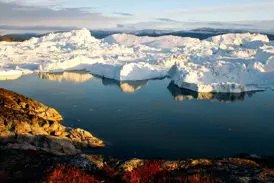 Goldene Abendsonne scheint auf die felsige Küste und die riesigen Eisberge im Ilulissat-Eisfjord in Westgrönland.