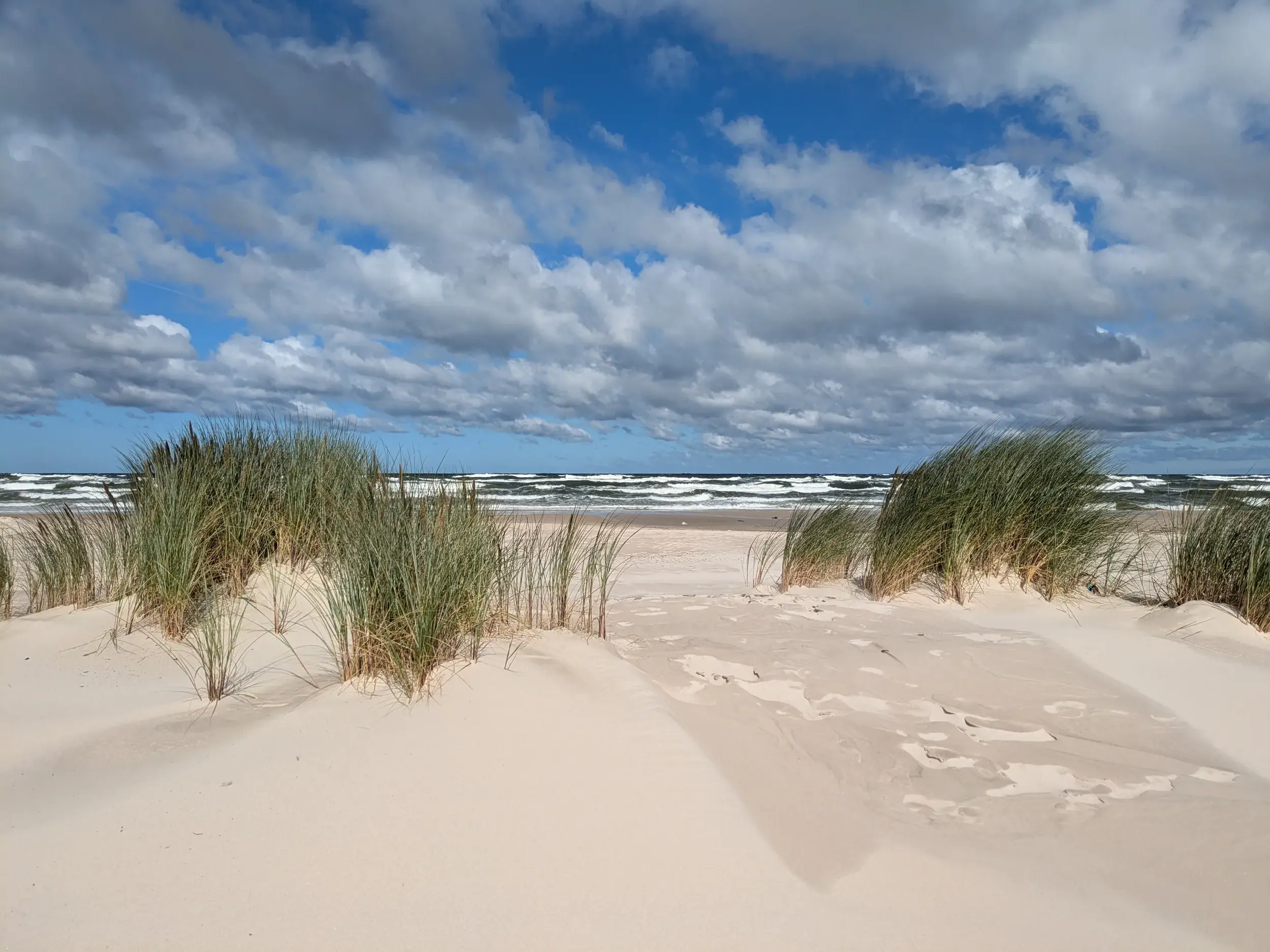 Blick über eine von Strandgras bewachsene Düne auf die wellenreiche Ostsee im Słowiński-Nationalpark in Polen.