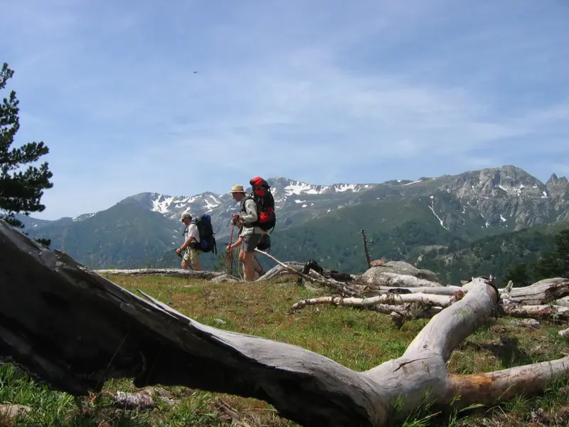 Zwei Wanderer mit Trekking-Ausrüstung auf dem GR20 auf Korsika, im Hintergrund eine Gebirgskette mit Schneeresten.