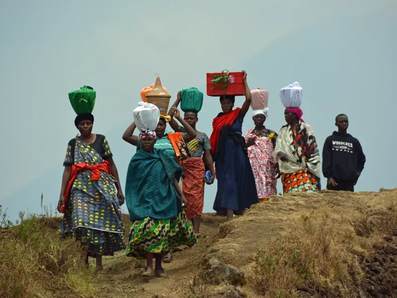 Gruppe einheimischer Frauen in bunten Kleidern trägt traditionell Körbe und Waren auf dem Kopf über einen erdigen Pfad in Ruanda.