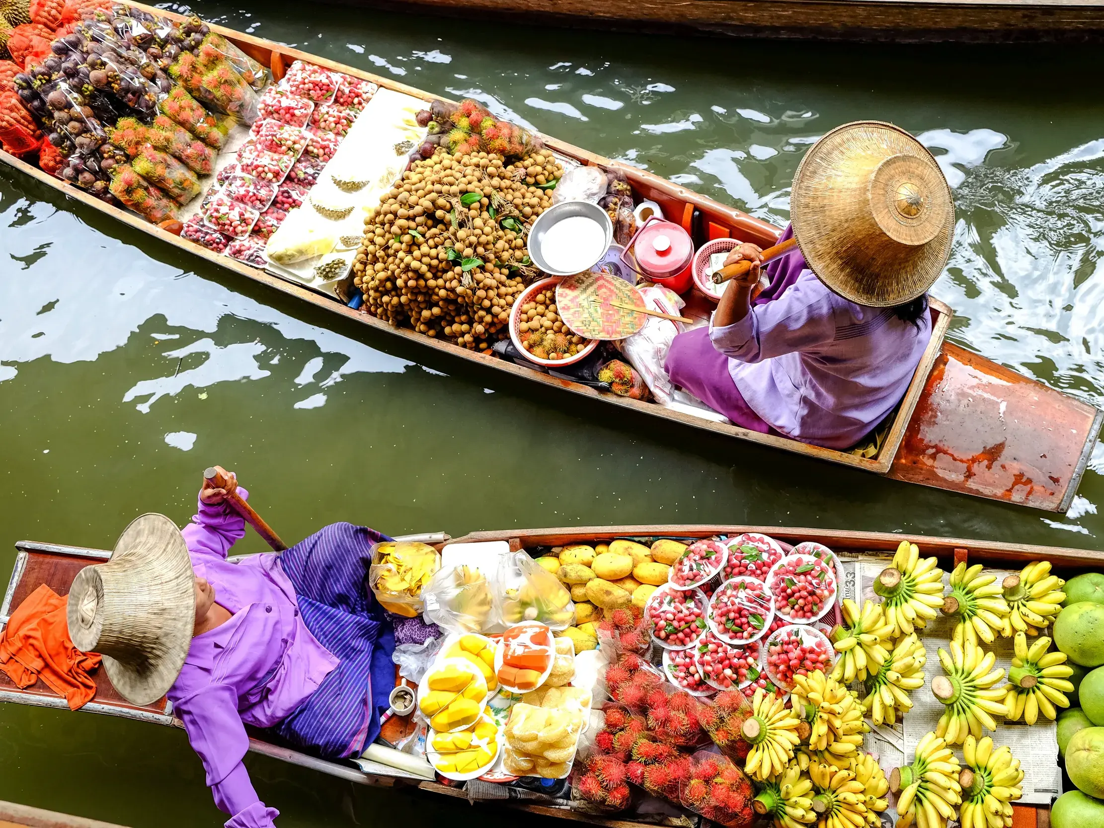 Händlerinnen in traditionellen Booten verkaufen bunte, exotische Früchte auf einem schwimmenden Markt im Mekongdelta in Vietnam.