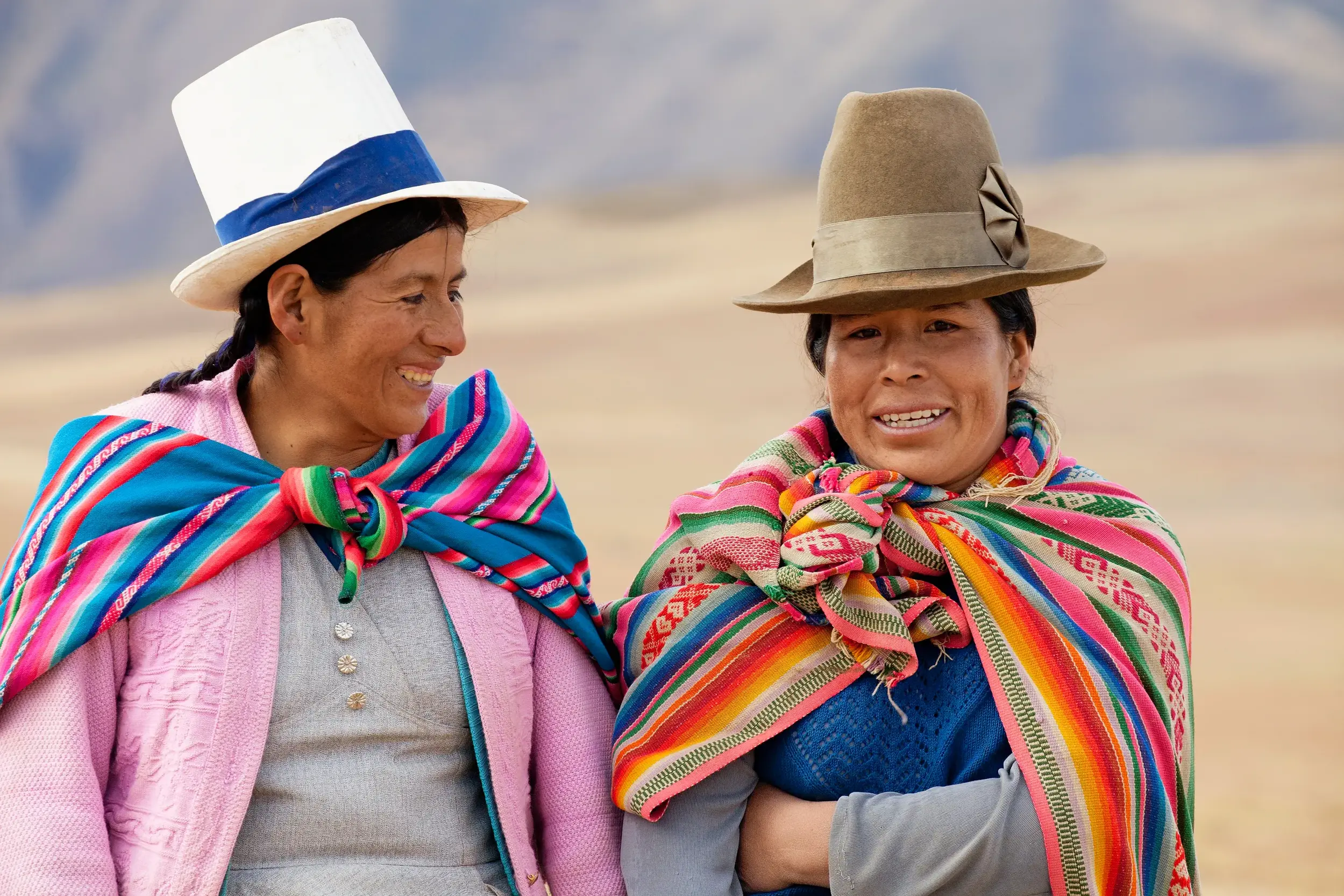 Zwei lächelnde Frauen in Peru in farbenfroher, traditioneller Anden-Tracht und mit typischen Hüten.