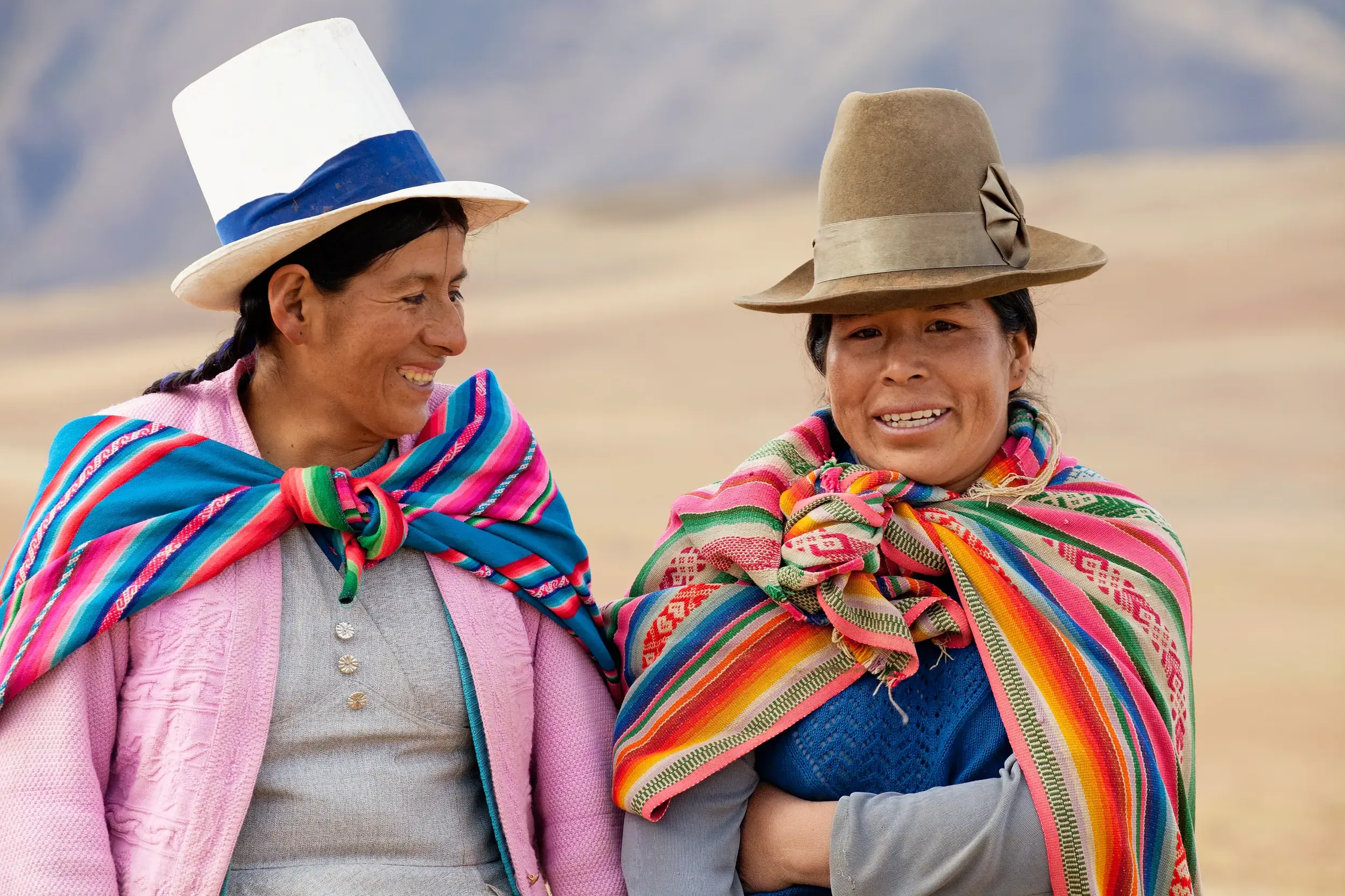 Zwei lächelnde Frauen in Peru in farbenfroher, traditioneller Anden-Tracht und mit typischen Hüten.