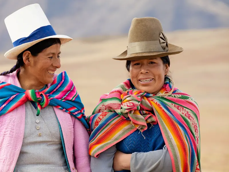 Zwei lächelnde Frauen in Peru in farbenfroher, traditioneller Anden-Tracht und mit typischen Hüten.