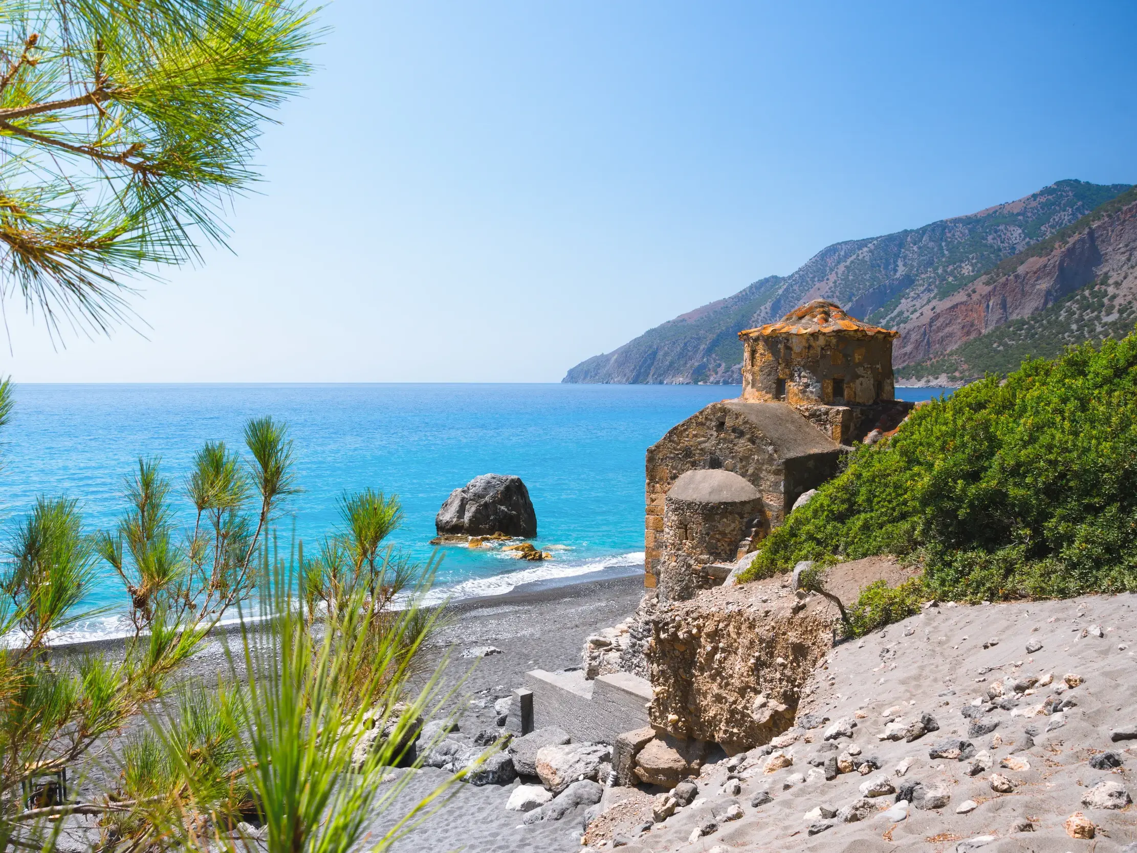 Die steinerne Kapelle Agios Pavlos aus dem 11. Jahrhundert am Strand mit türkisblauem Meer an der Südküste von Kreta.