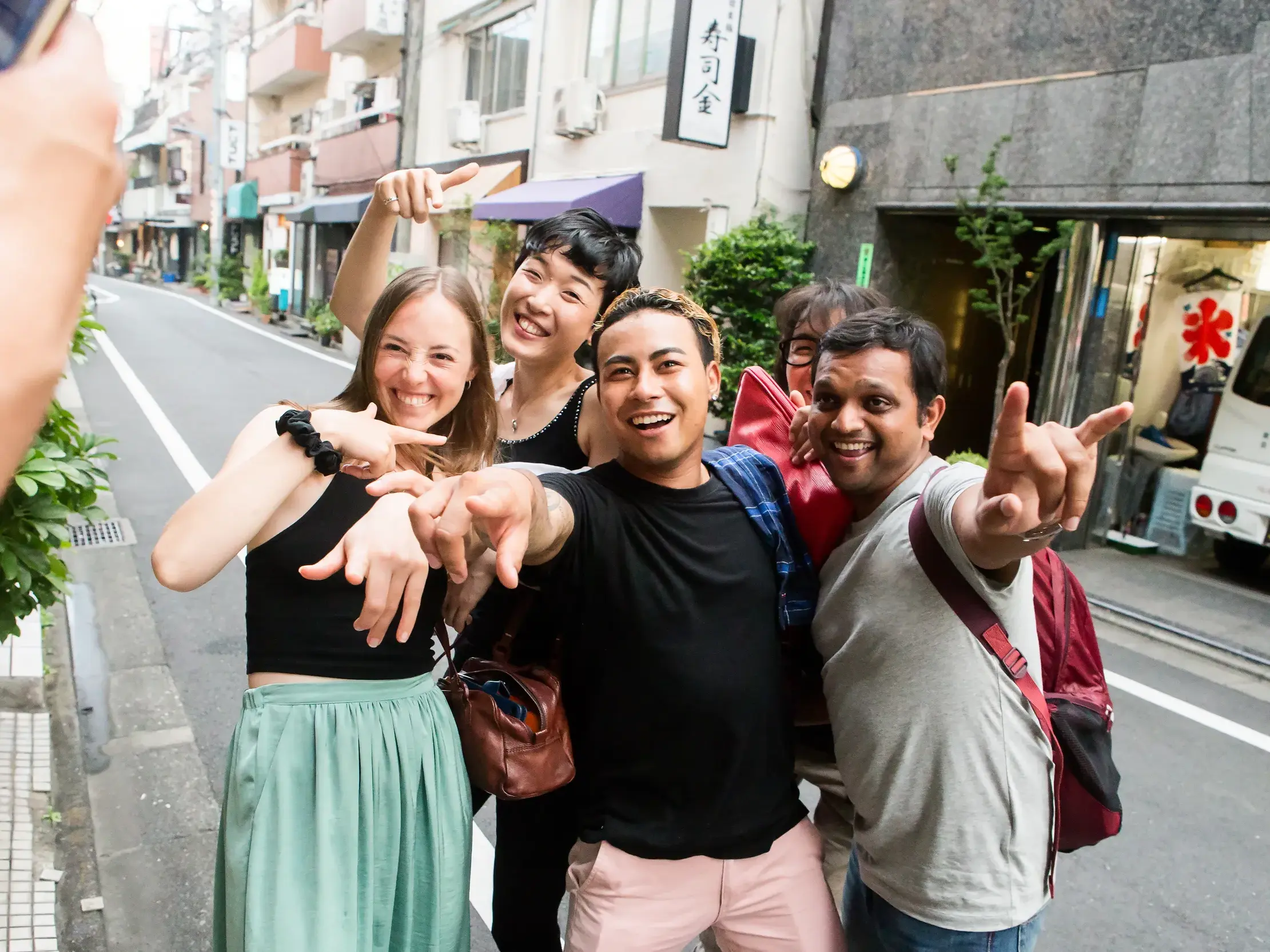 Eine Gruppe junger Leute auf einer geführten Rundreise posiert lachend für ein Foto in einer Straße in Tokio.