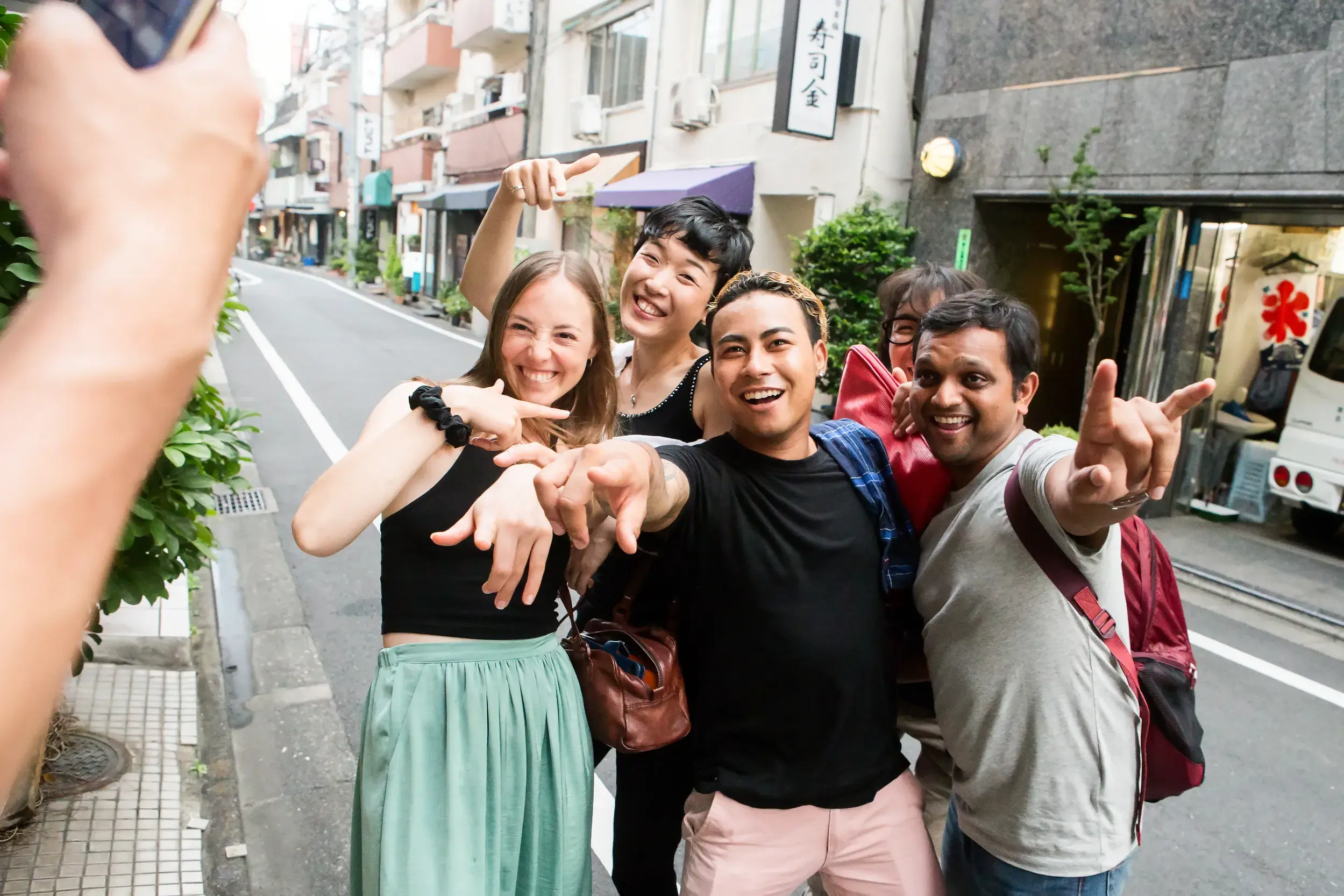 Eine Gruppe junger Leute auf einer geführten Rundreise posiert lachend für ein Foto in einer Straße in Tokio.