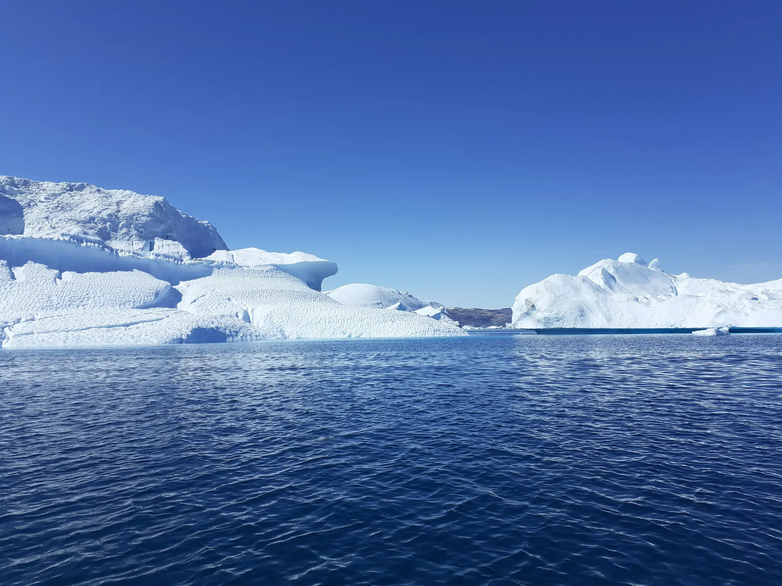 Gewaltige Eisberge treiben unter klarem Himmel im tiefblauen Wasser des Sermilik-Fjords in Ostgrönland.