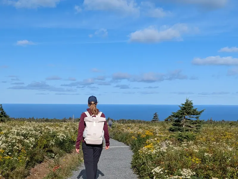 Wanderin mit Rucksack auf dem Skyline Trail im Cape Breton Highlands Nationalpark mit weitem Panoramablick auf den Atlantik.