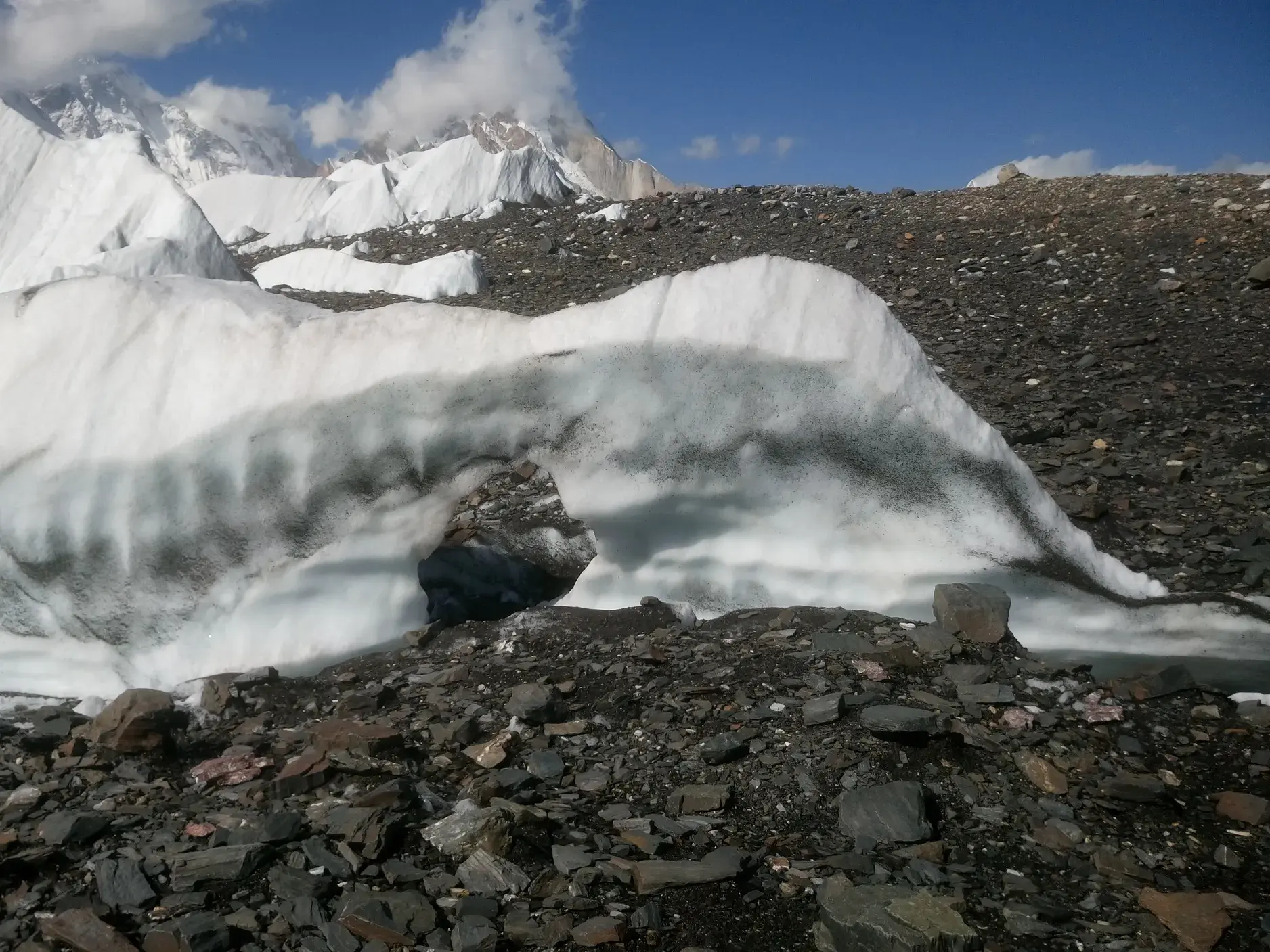 Natürliche Eisformation mit einem Bogen auf dem schuttbedeckten Baltoro-Gletscher vor der Kulisse der Karakorum-Gipfel.