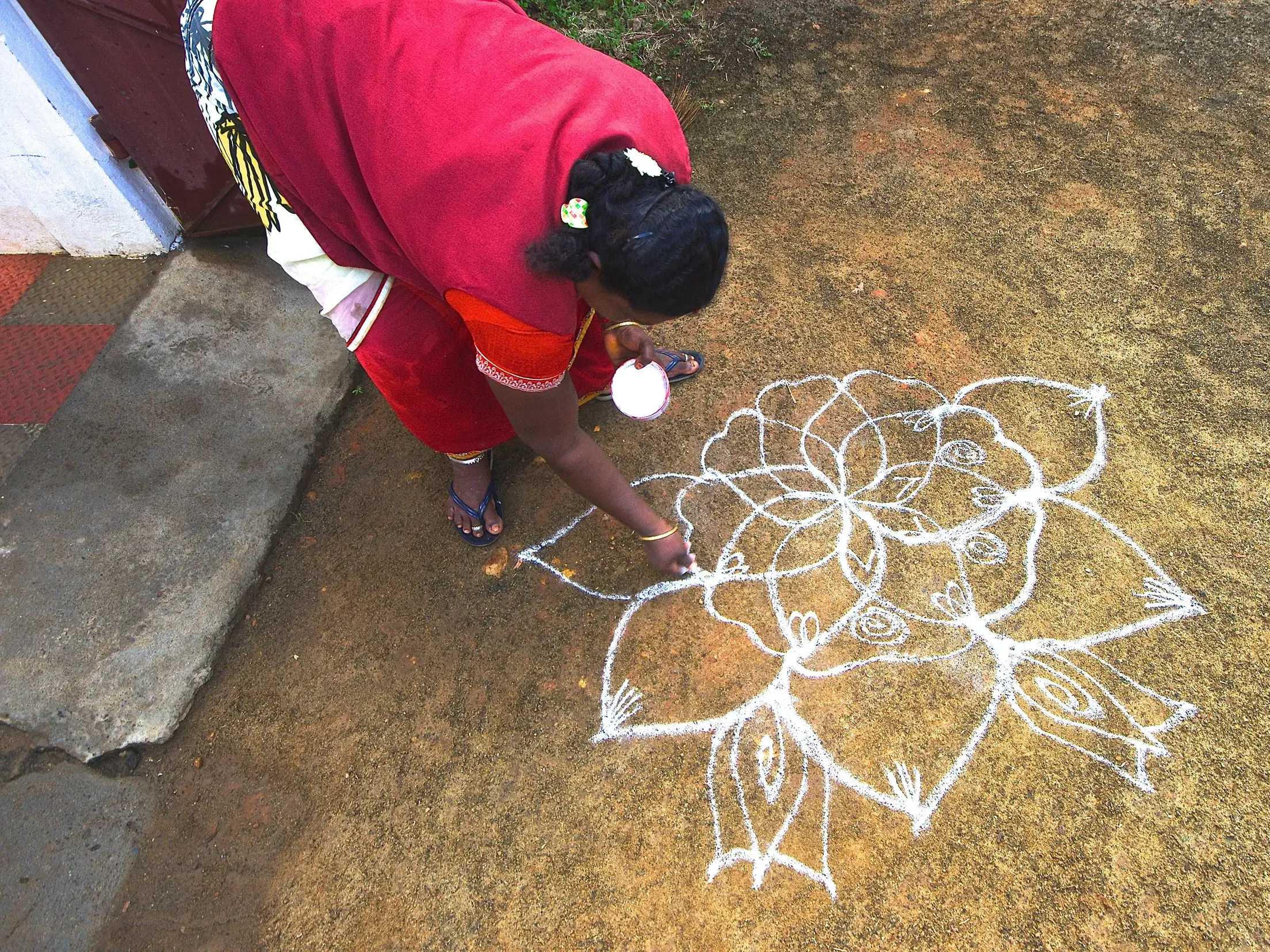 Auf einer Studienreise in Südindien: Eine Frau im Sari malt mit weißem Reismehl ein kunstvolles Kolam auf den Boden.