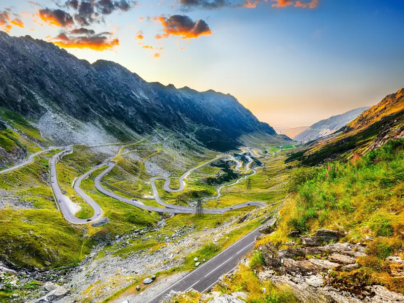 Spektakuläre Passstraße schlängelt sich durch das grüne Bergpanorama der rumänischen Karpaten im warmen Abendlicht.