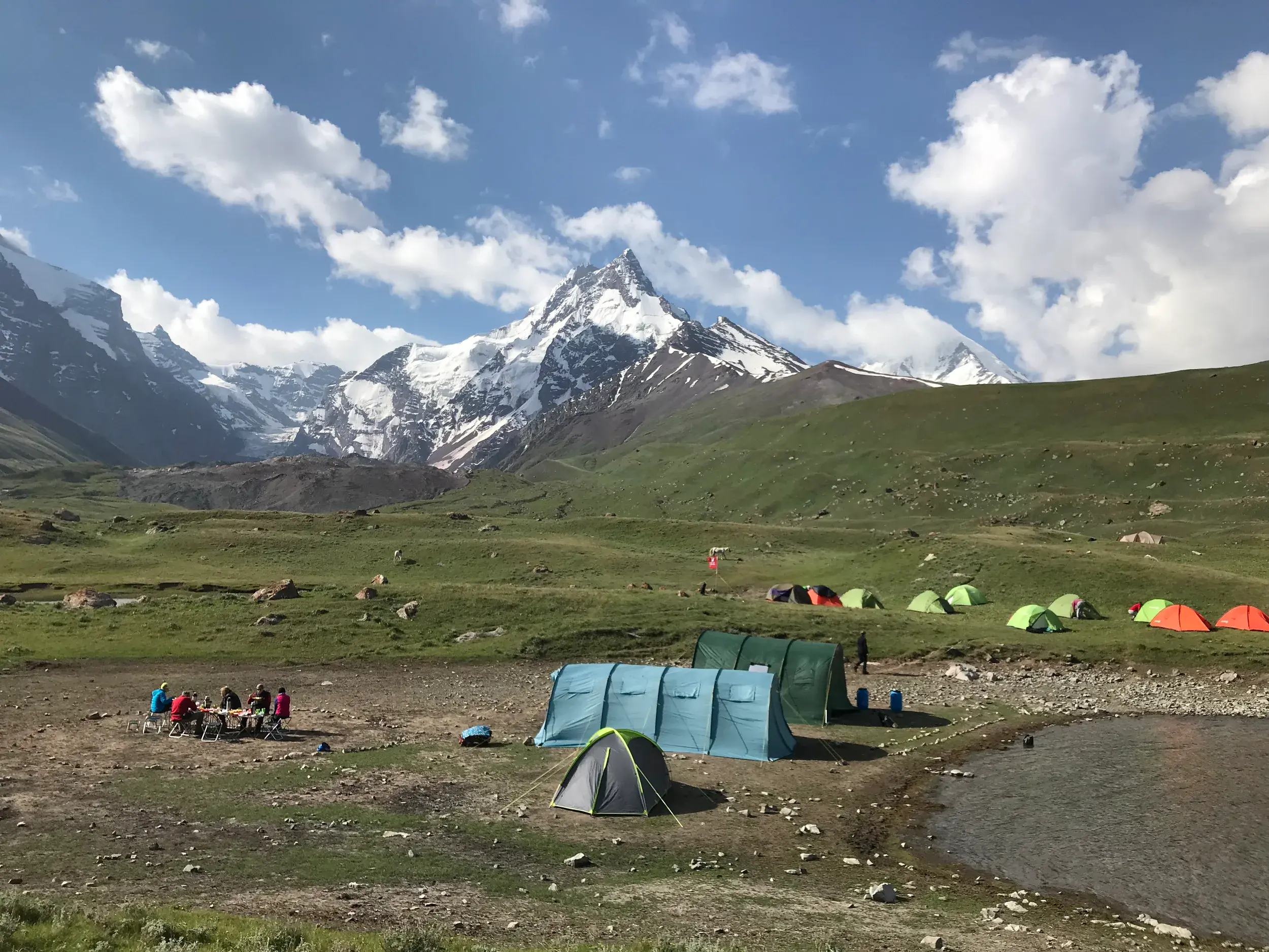 Hauser-Reisegruppe zeltet am Yashilkul-See in Tadschikistan mit Blick auf die schneebedeckten, majestätischen Pamir-Gipfel.