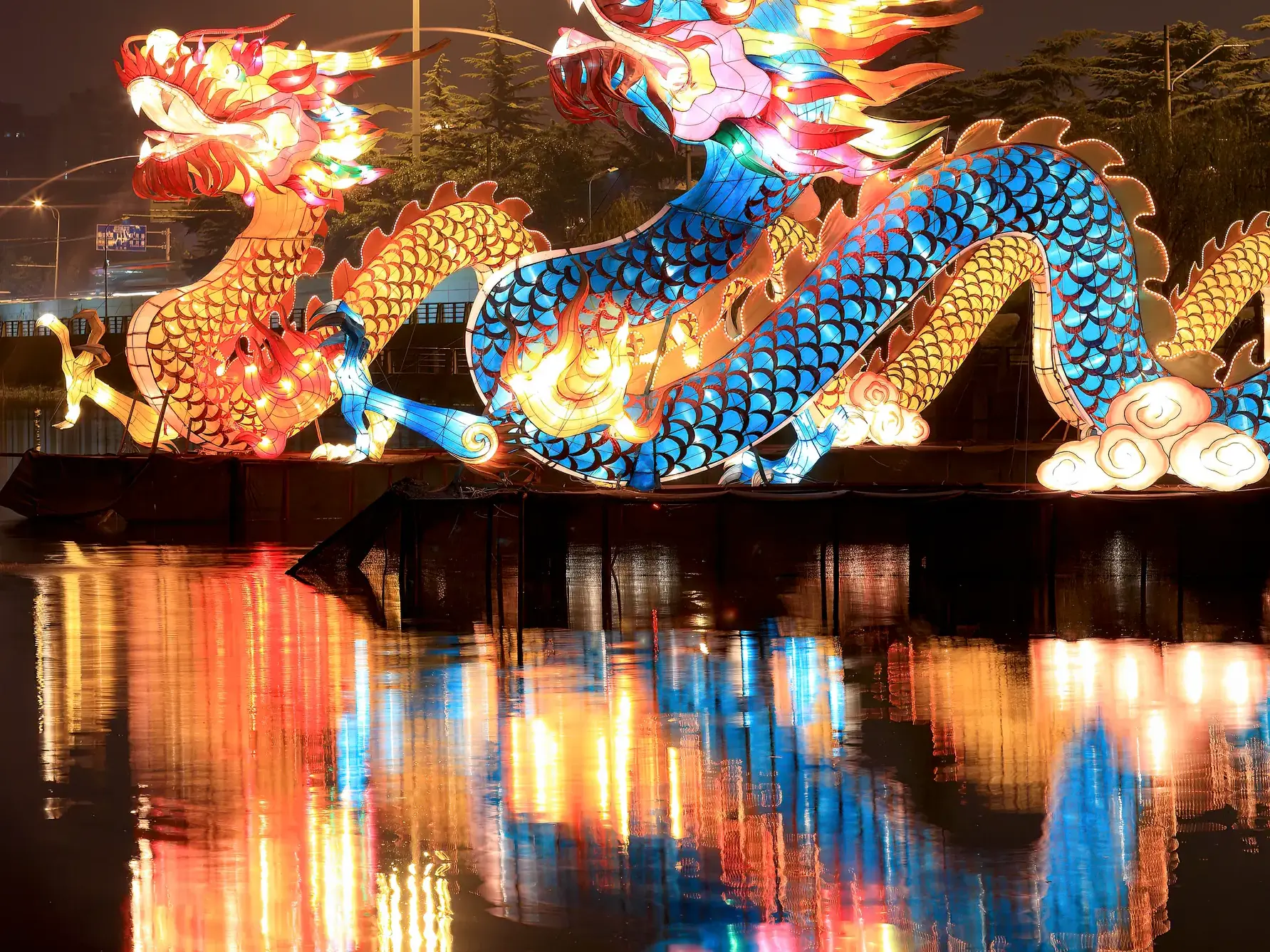 Zwei kunstvolle chinesische Drachenlaternen in Rot und Blau leuchten nachts auf einem See und spiegeln sich farbenprächtig im Wasser.