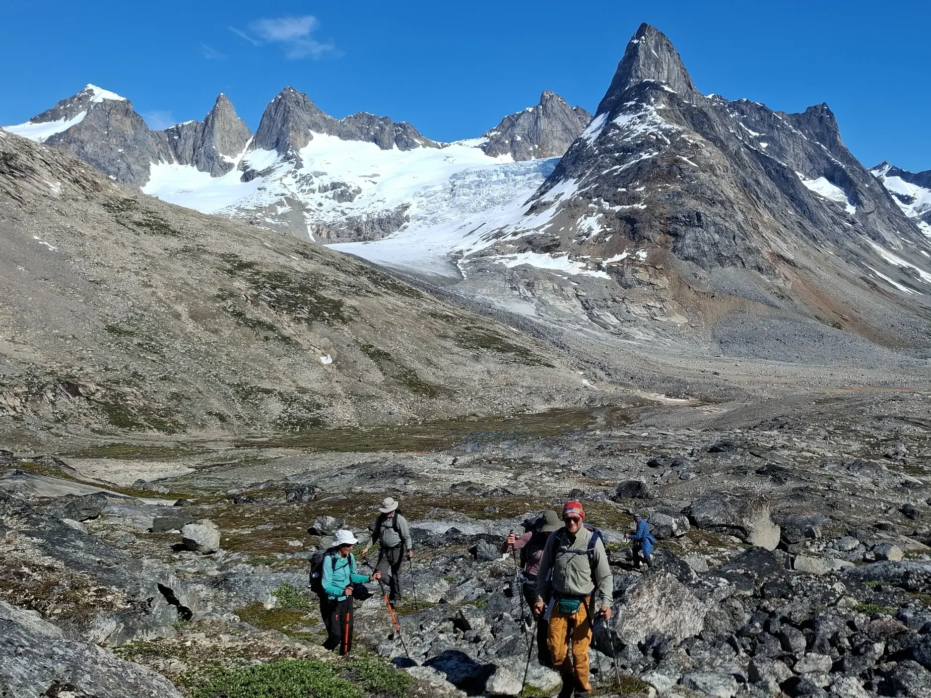 Eine Trekking-Gruppe wandert durch eine karge Felslandschaft in Ostgrönland mit Blick auf die Gletscher am Niialigaq.