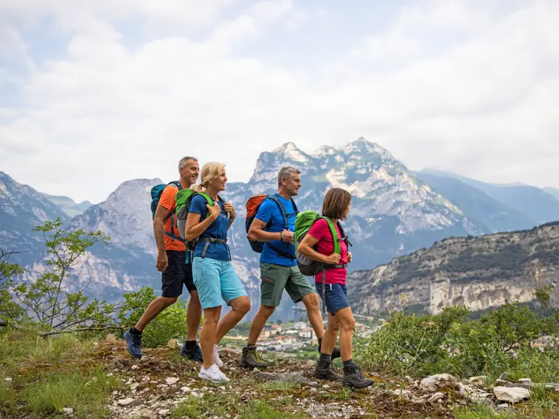 Vierköpfige Wandergruppe auf einem Bergpfad im Trentino mit Blick auf das Tal und die Brenta-Dolomiten im Hintergrund.
