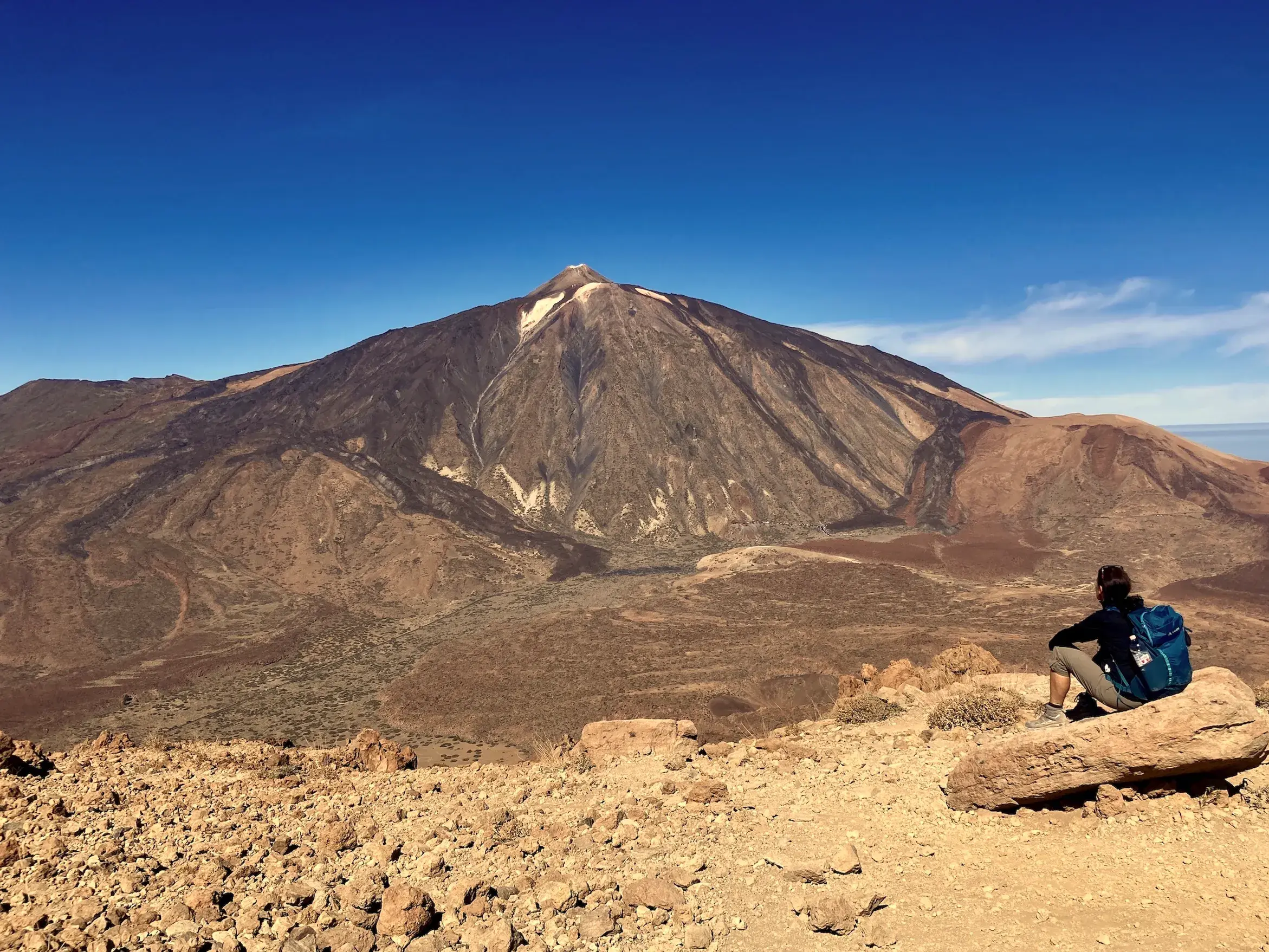 Wanderer mit Rucksack bei einer Pause auf einem Felsen mit Panoramablick auf den Vulkan Teide im Nationalpark Las Cañadas.