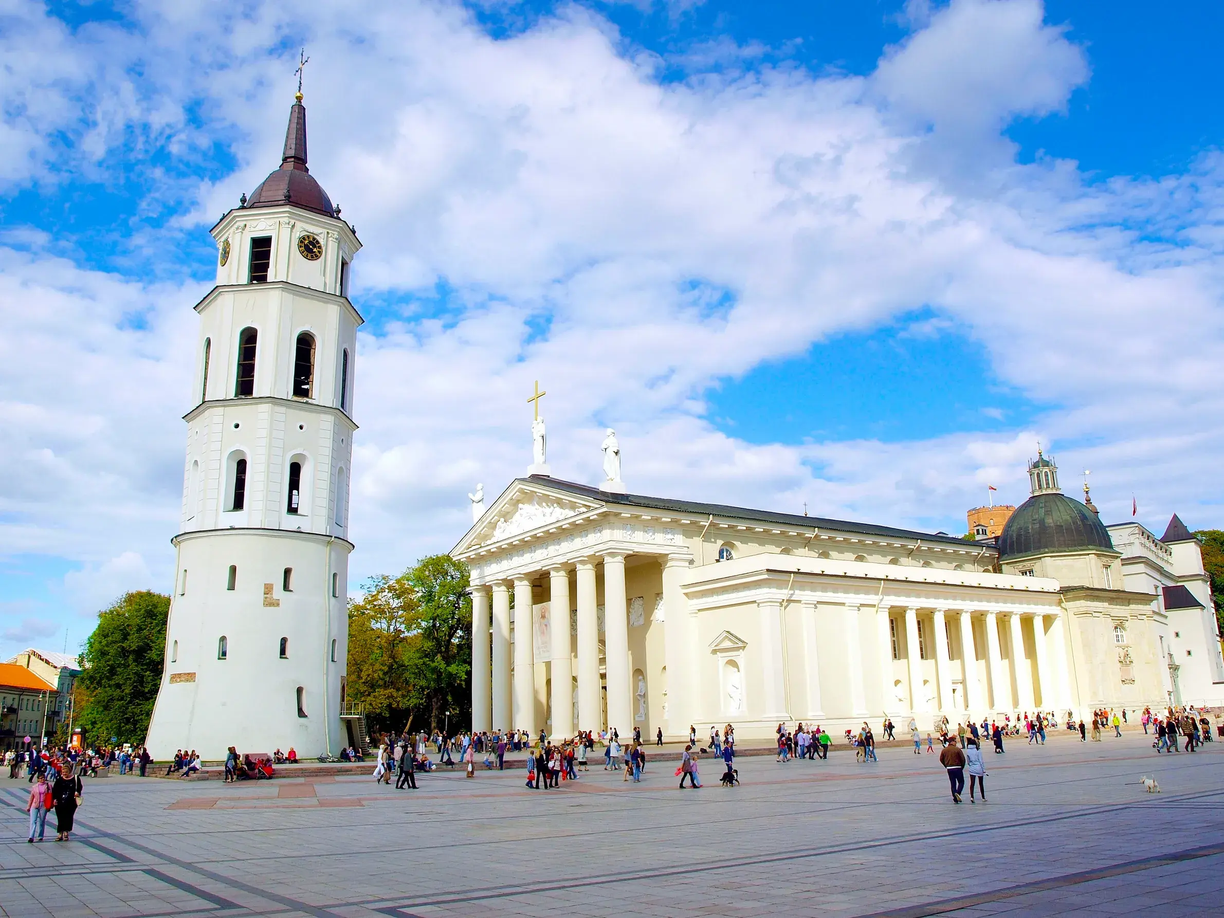 Die strahlend weiße Kathedrale von Vilnius mit ihrem Glockenturm auf dem belebten Kathedralenplatz unter blauem Himmel.