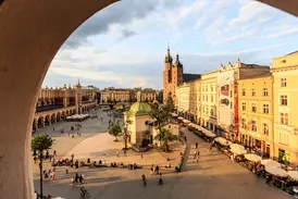 Blick durch einen Bogen auf den belebten Hauptring in Krakau mit den Tuchhallen und der Marienkirche in der Abendsonne.