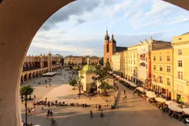 Blick durch einen Bogen auf den belebten Hauptring in Krakau mit den Tuchhallen und der Marienkirche in der Abendsonne.