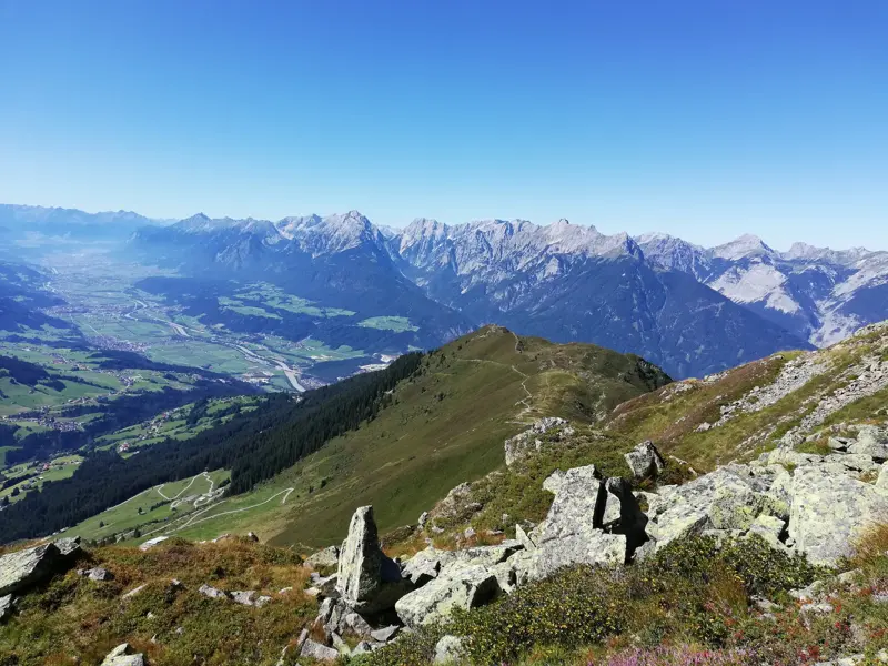 Sonnige Panoramasicht von einem Wanderweg über das weite Zillertal auf die schroffen Gipfel der Zillertaler Alpen.