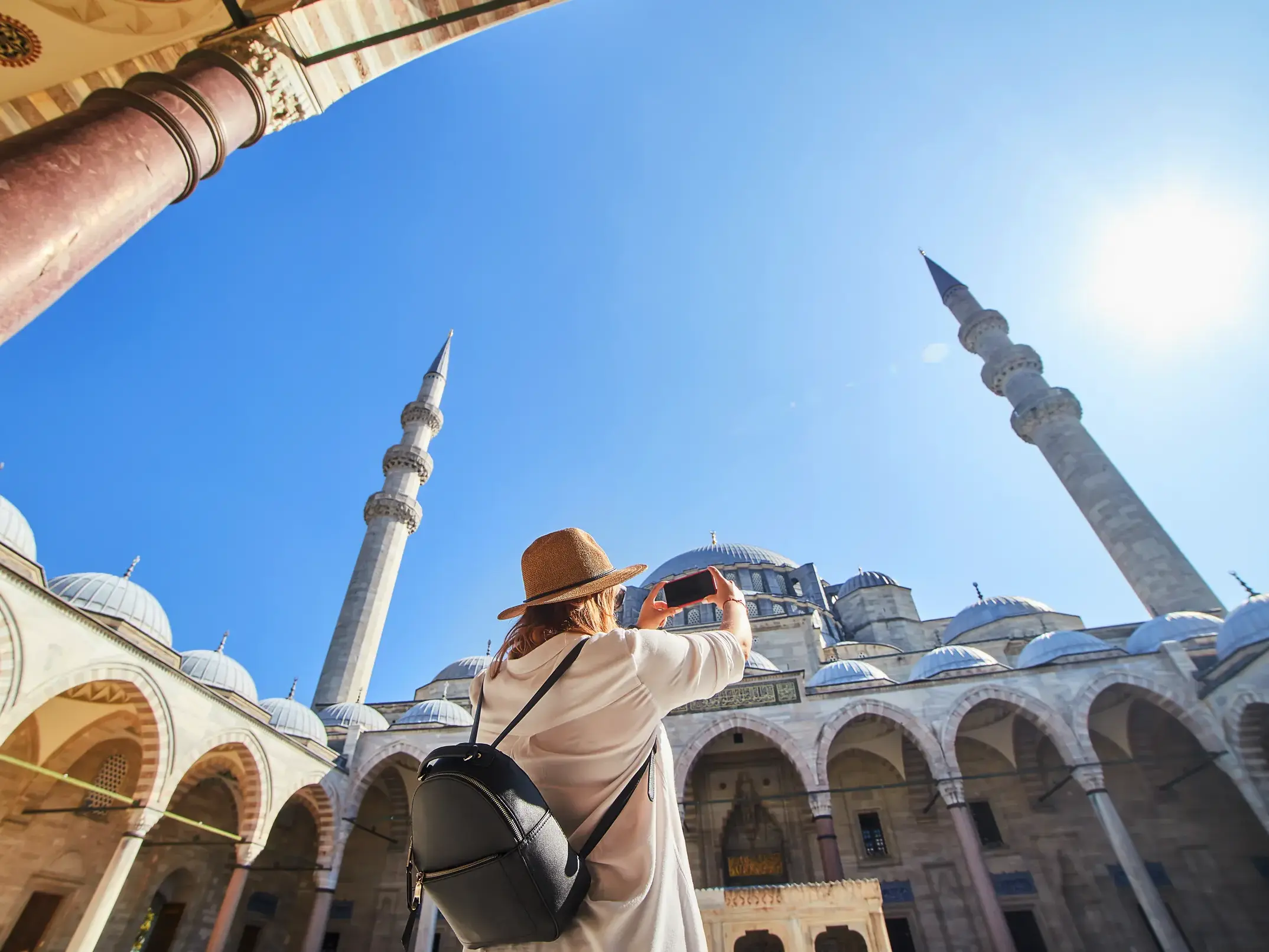 Eine Reisende mit Hut macht im Innenhof ein Foto von der prachtvollen Süleymaniye-Moschee in Istanbul bei Sonnenschein.