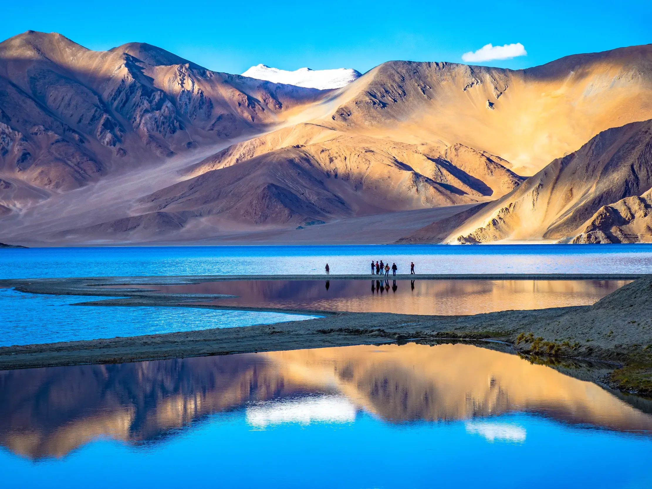 Eine Reisegruppe bestaunt die Spiegelung der Himalaya-Berge im kristallklaren Wasser des Pangong-Sees in Ladakh.
