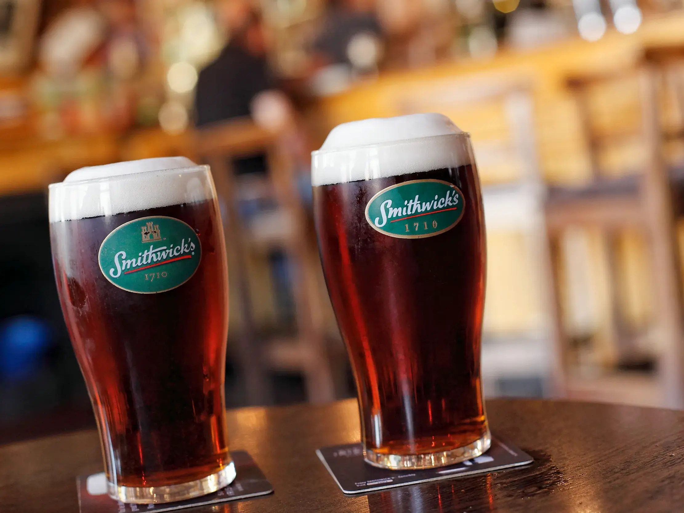 Zwei frisch gezapfte Pints des irischen Biers Smithwick's auf einem Holztisch in einem gemütlichen Pub in Irland.
