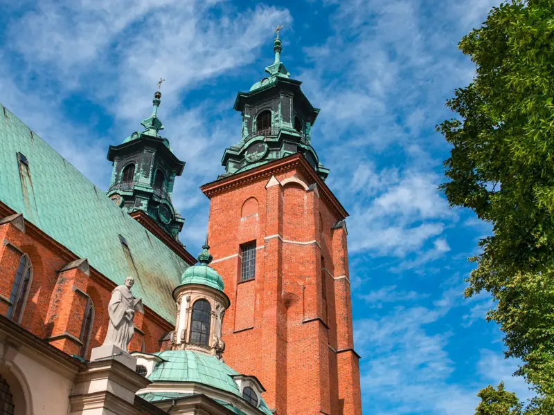 Die roten Backsteintürme der Krönungskirche in Gniezno mit grünen Kupferdächern ragen in den blauen Himmel.