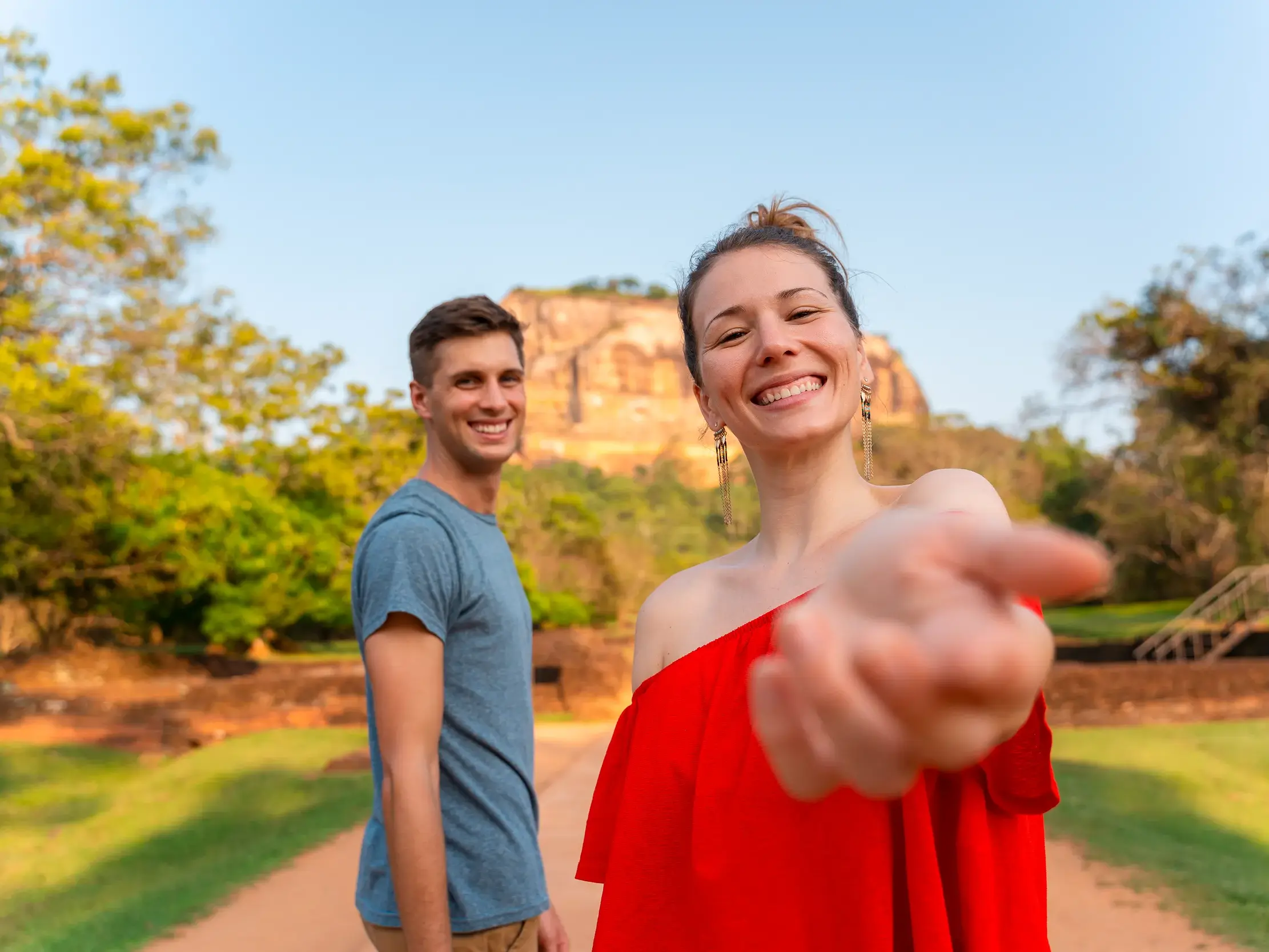 Eine junge Frau reicht ihre Hand auf einer Gruppenreise für junge Leute vor dem berühmten Sigiriya-Felsen in Sri Lanka.