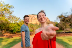 Eine junge Frau reicht ihre Hand auf einer Gruppenreise für junge Leute vor dem berühmten Sigiriya-Felsen in Sri Lanka.