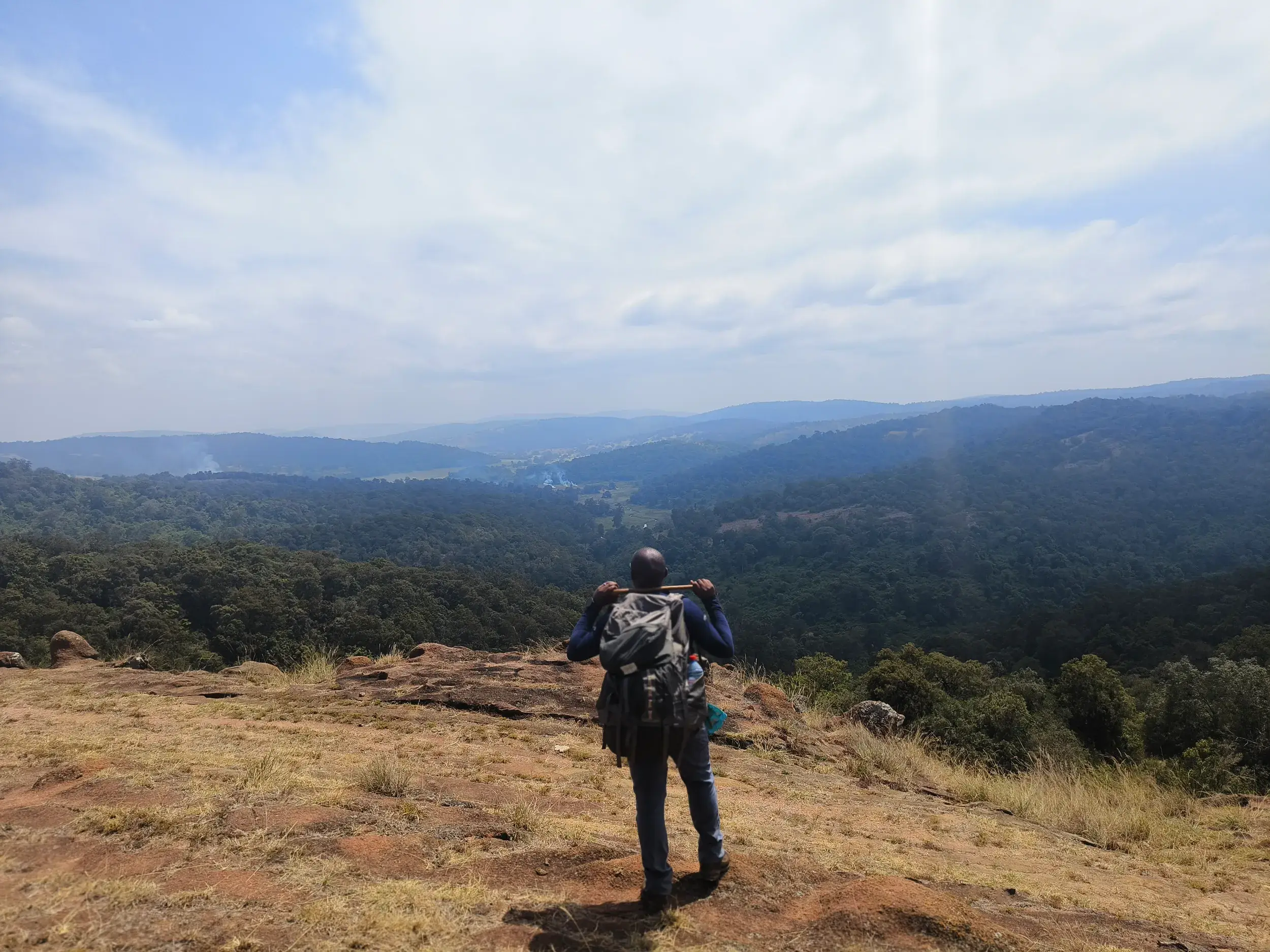 Ein Trekker mit Rucksack steht auf einem Felsplateau und blickt über das grüne Tal des Großen Afrikanischen Grabenbruchs in Kenia.