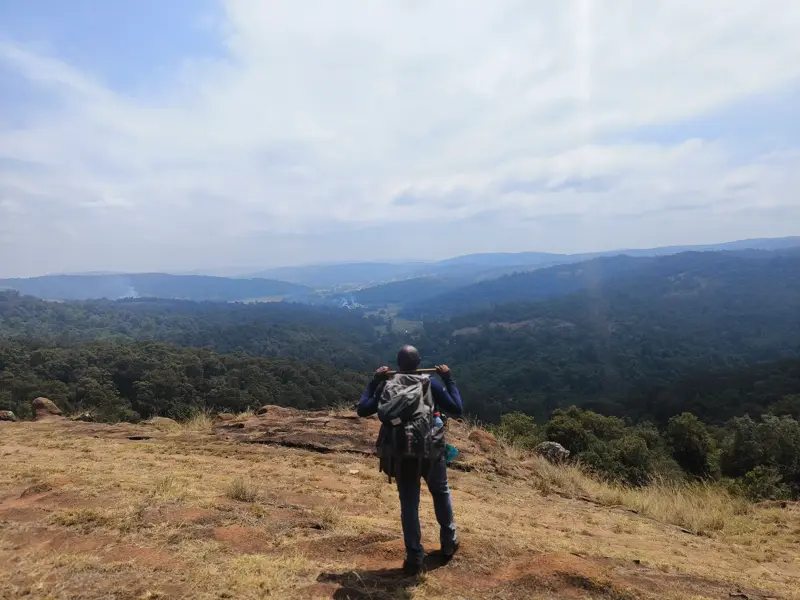 Ein Trekker mit Rucksack steht auf einem Felsplateau und blickt über das grüne Tal des Großen Afrikanischen Grabenbruchs in Kenia.